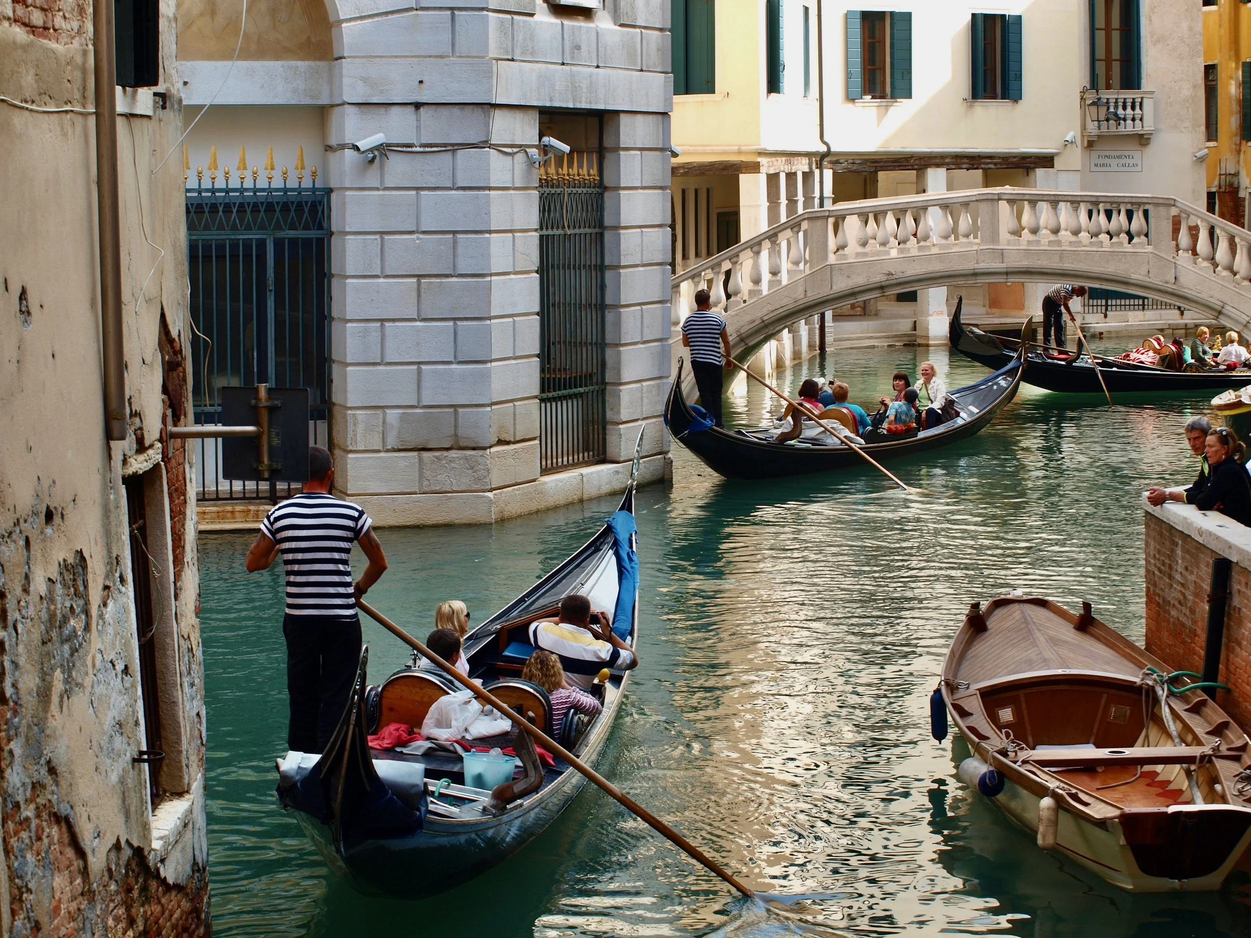 Gondoleurs naviguant sur un canal à Venise, avec bâtiments anciens et pont en arrière-plan.