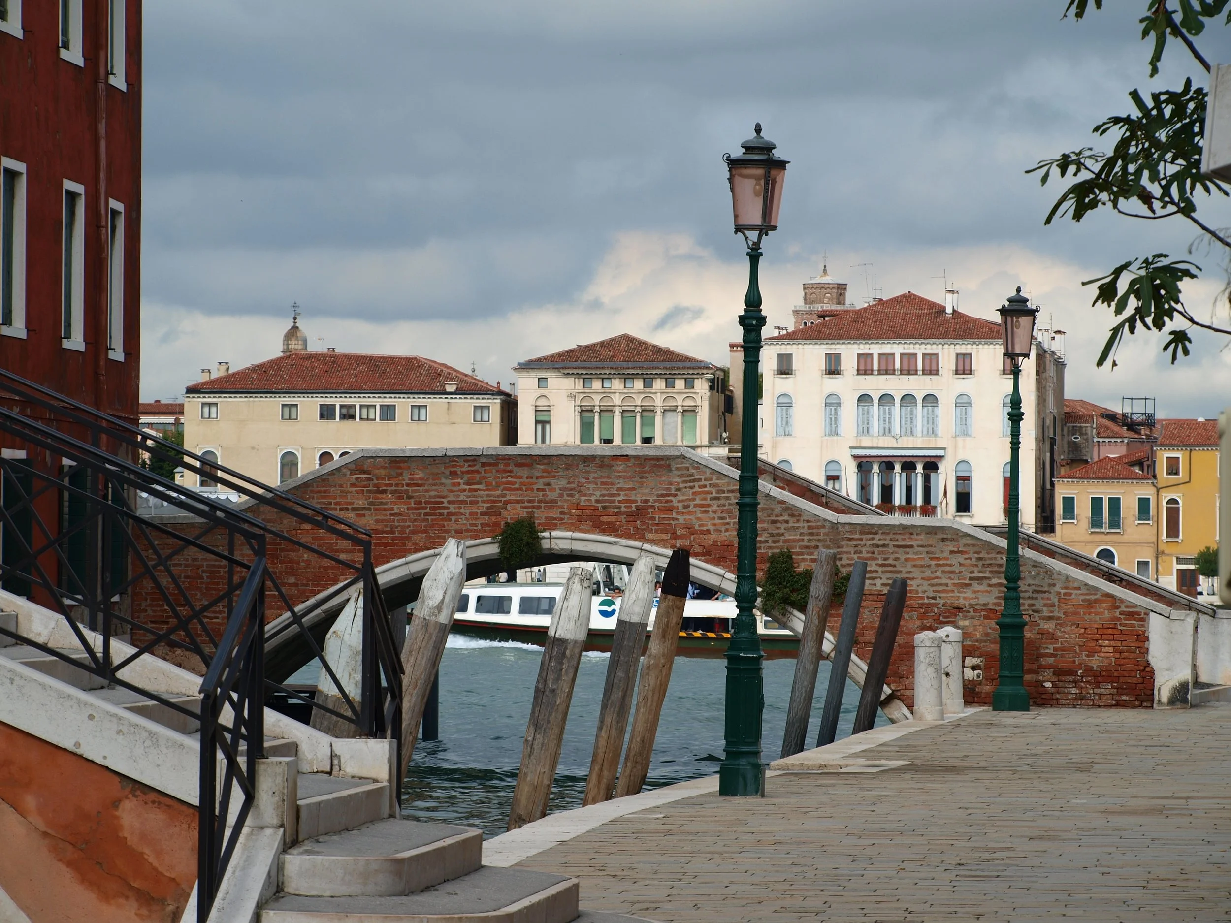 Une terrasse au bord d'un canal avec des lampadaires, des bâtiments colorés à l'arrière-plan et un ciel nuageux.