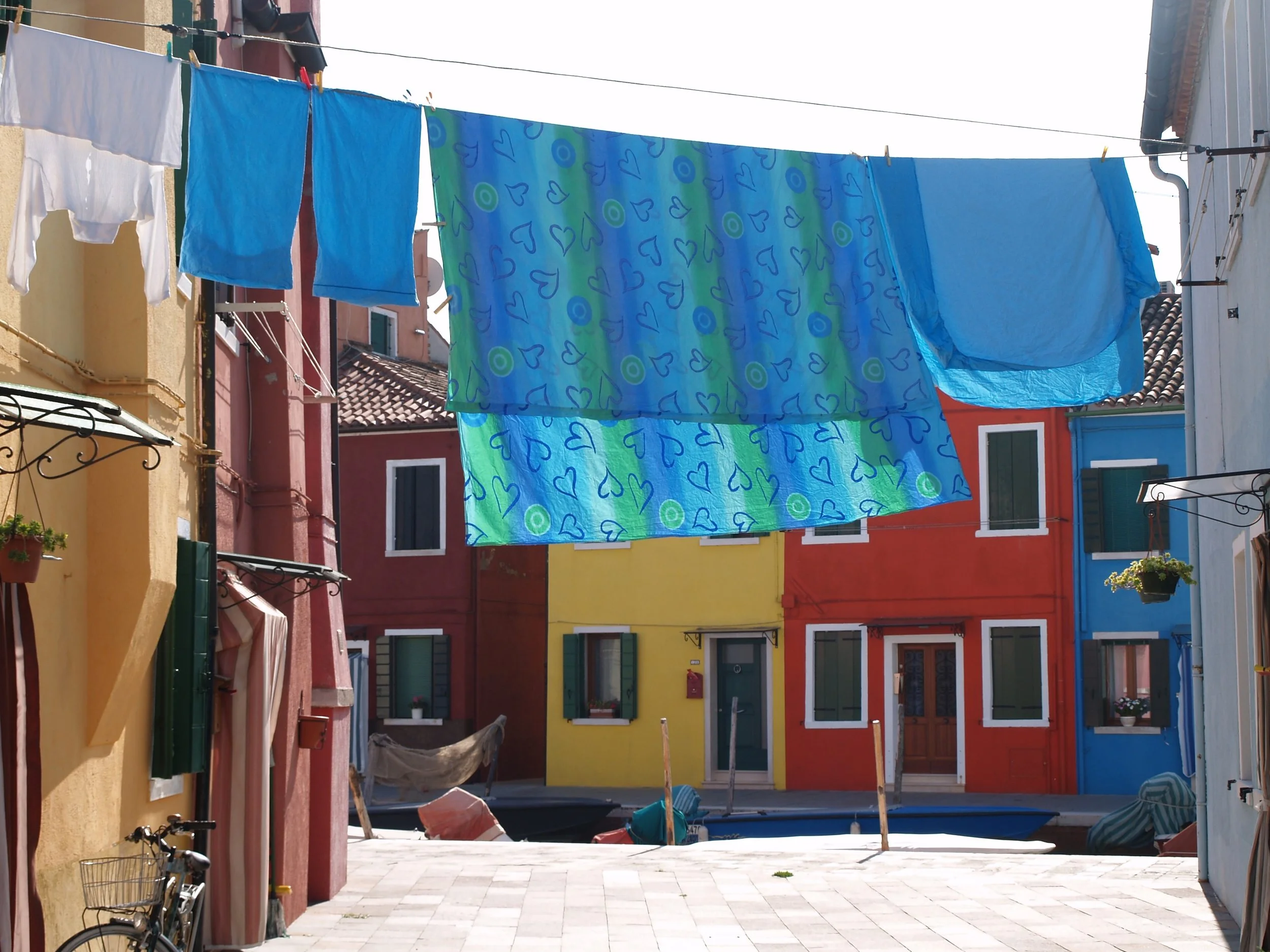 Lavage de vêtements suspendus à une corde à linge dans une rue colorée avec des bâtiments peints en jaune, rouge, orange, vert et bleu.