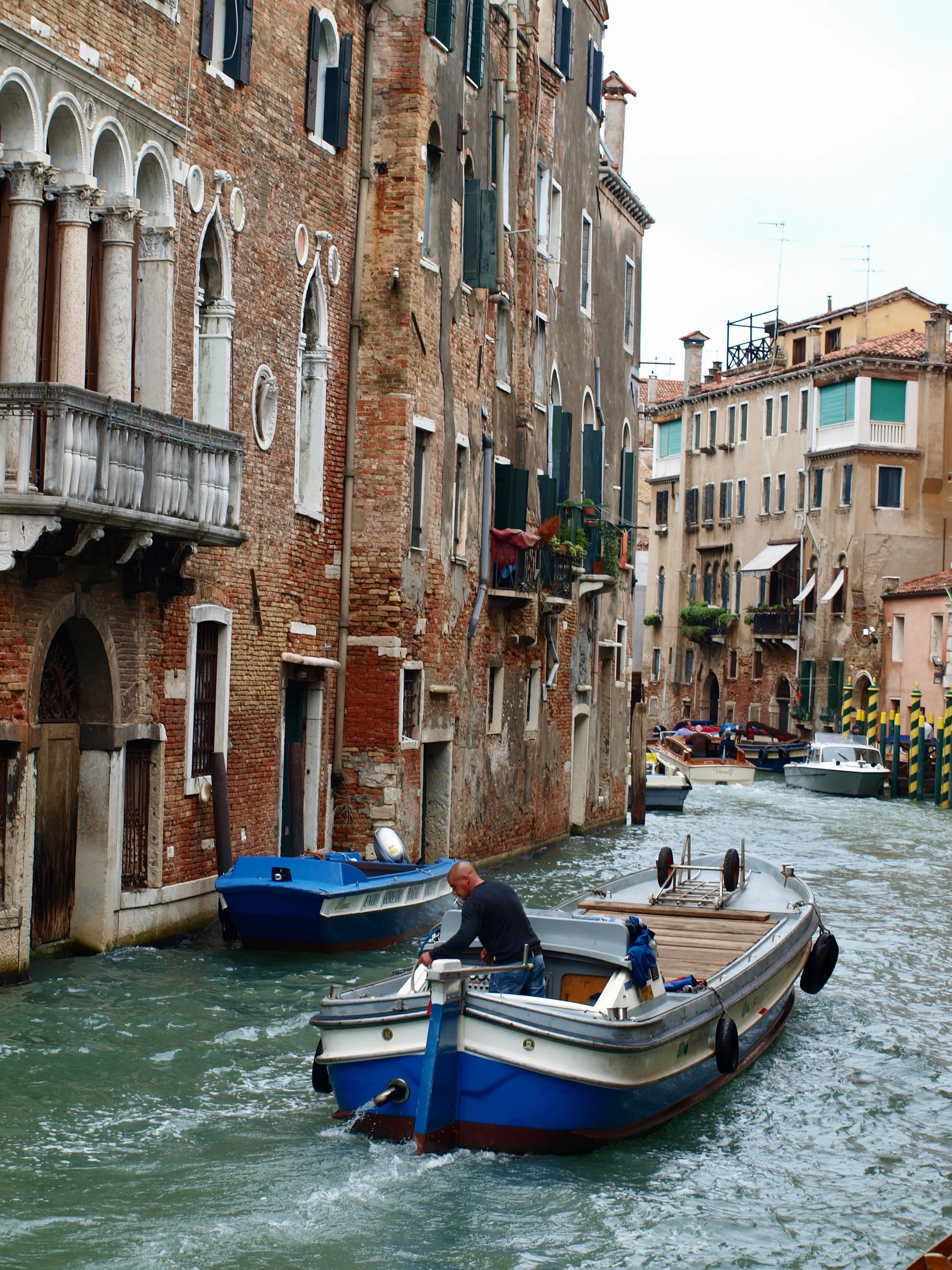 Une scène urbaine à Venise avec des bateaux naviguant dans un canal, entouré de bâtiments anciens en briques et en pierre.