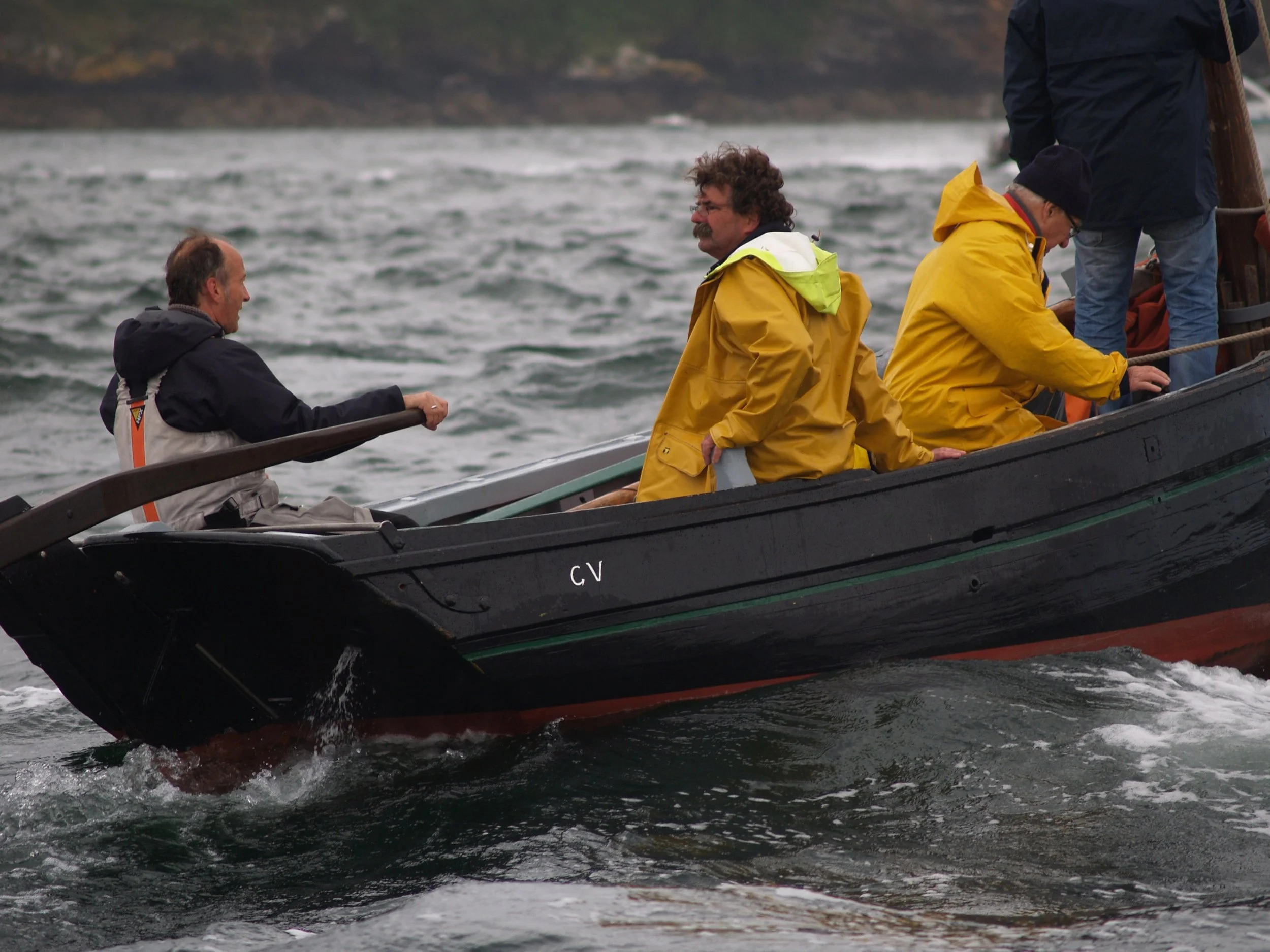 Quatre personnes en vêtements de pluie naviguant sur un bateau en mer par temps nuageux.