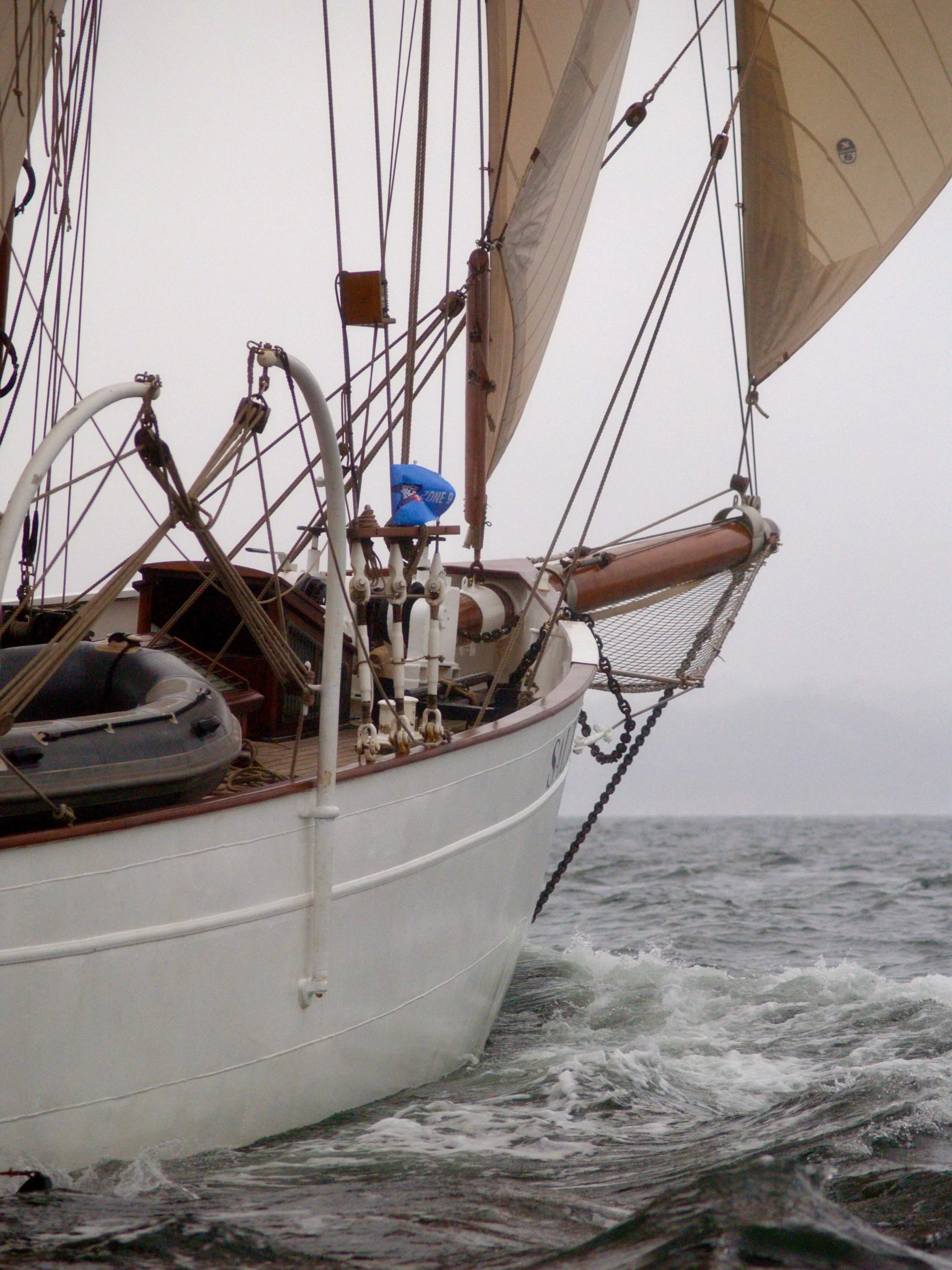Un voilier naviguant sur la mer, vue partielle de la proue avec cordages et voiles, par temps nuageux.