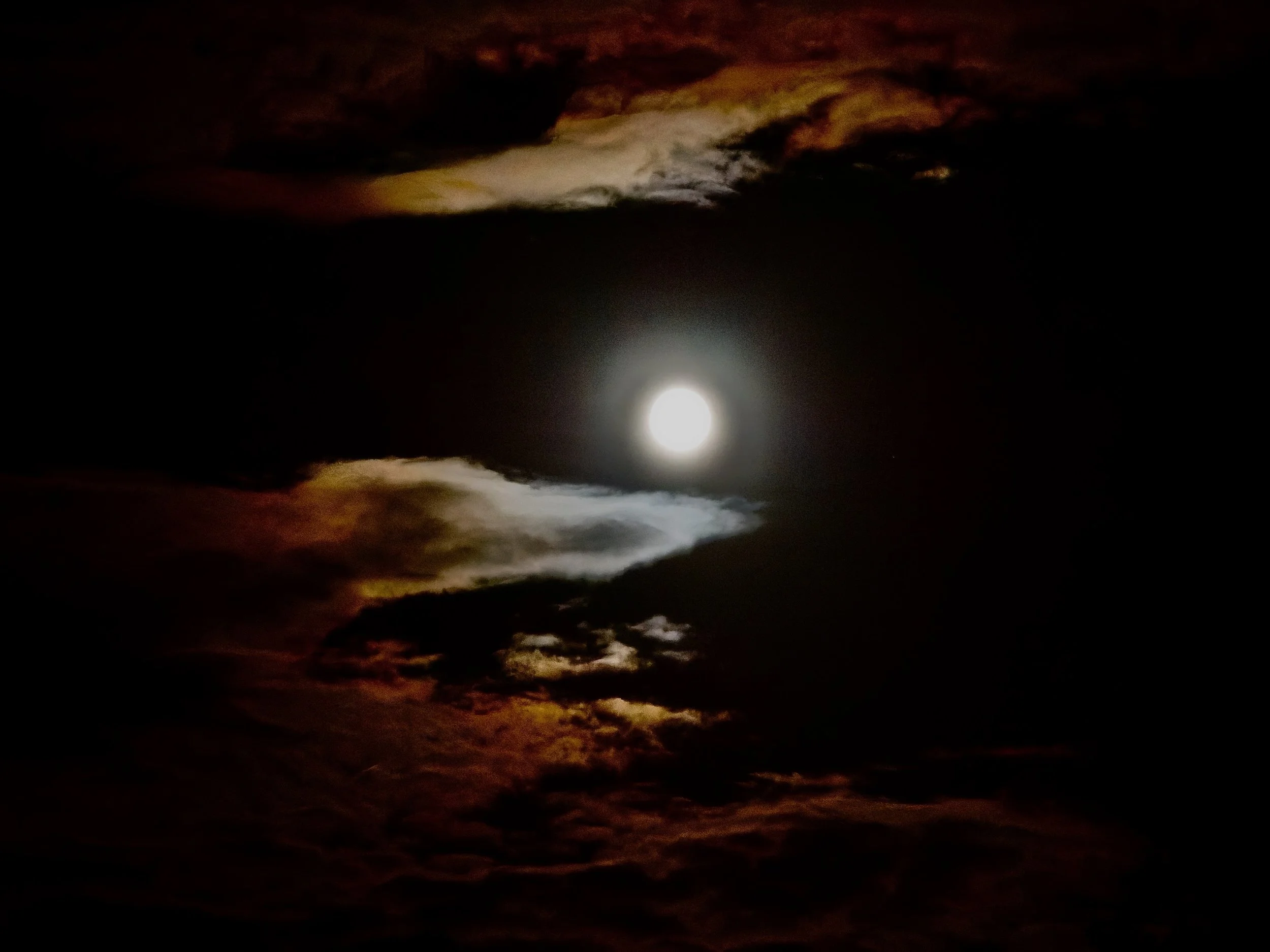 Une pleine lune brillante dans un ciel nuageux sombre avec des nuages dorés et orangés.