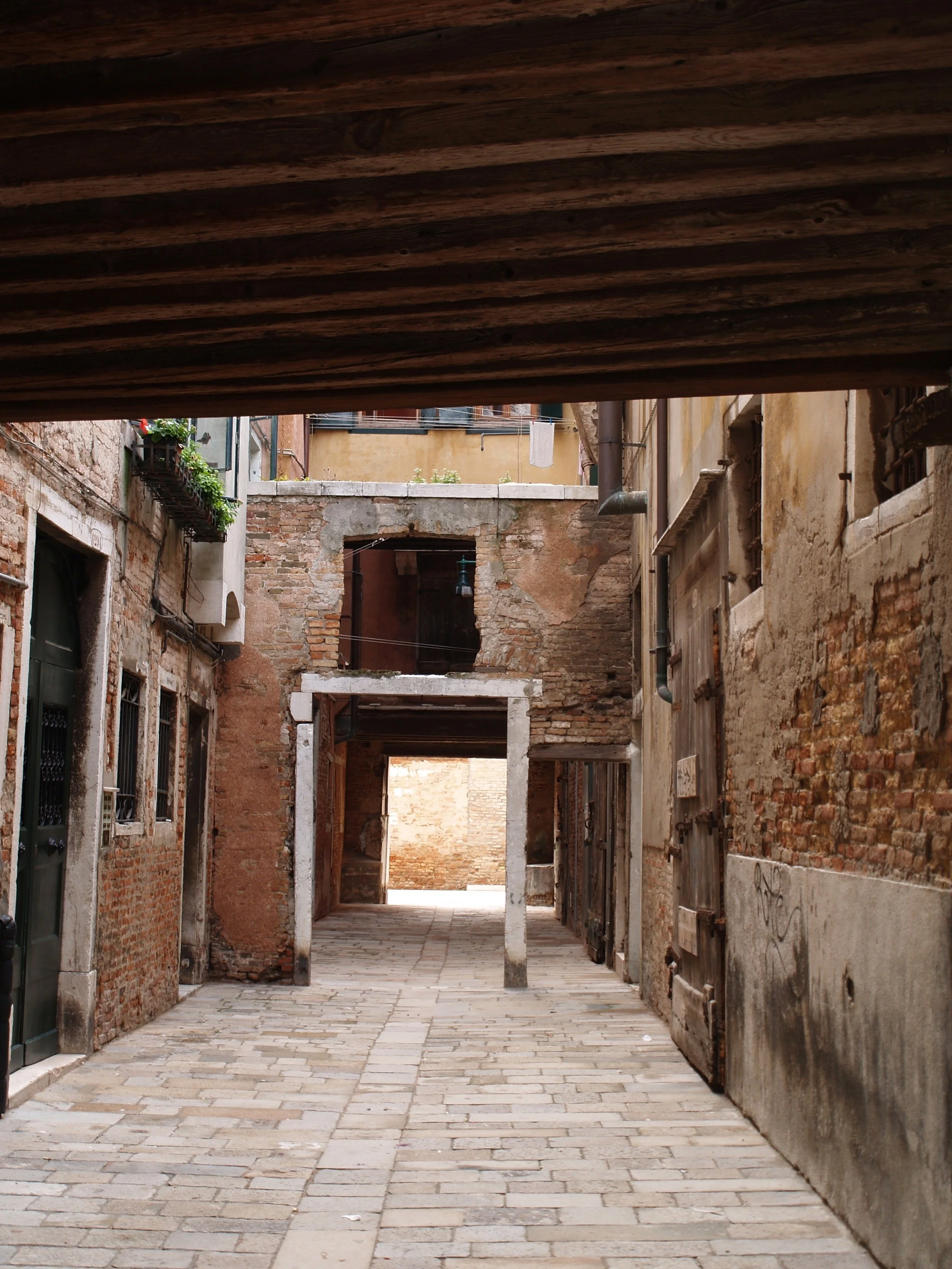 Une rue pavée bordée de bâtiments en briques et en plâtre, avec des fenêtres ornées de fleurs et une arche en pierre à l'arrière-plan.