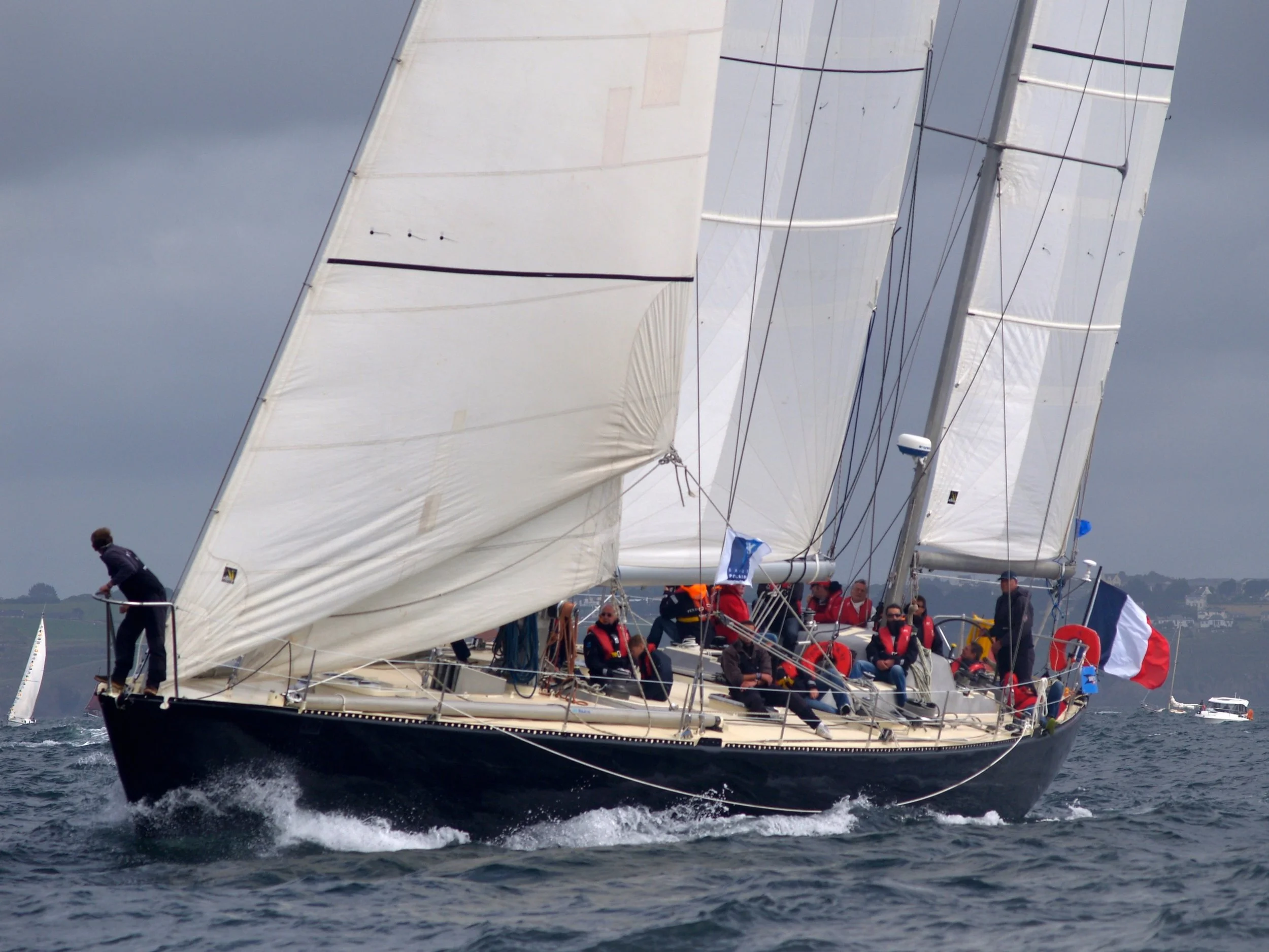 Un voilier avec plusieurs marins naviguant sur l'eau, avec de grands voiles blancs déployés.