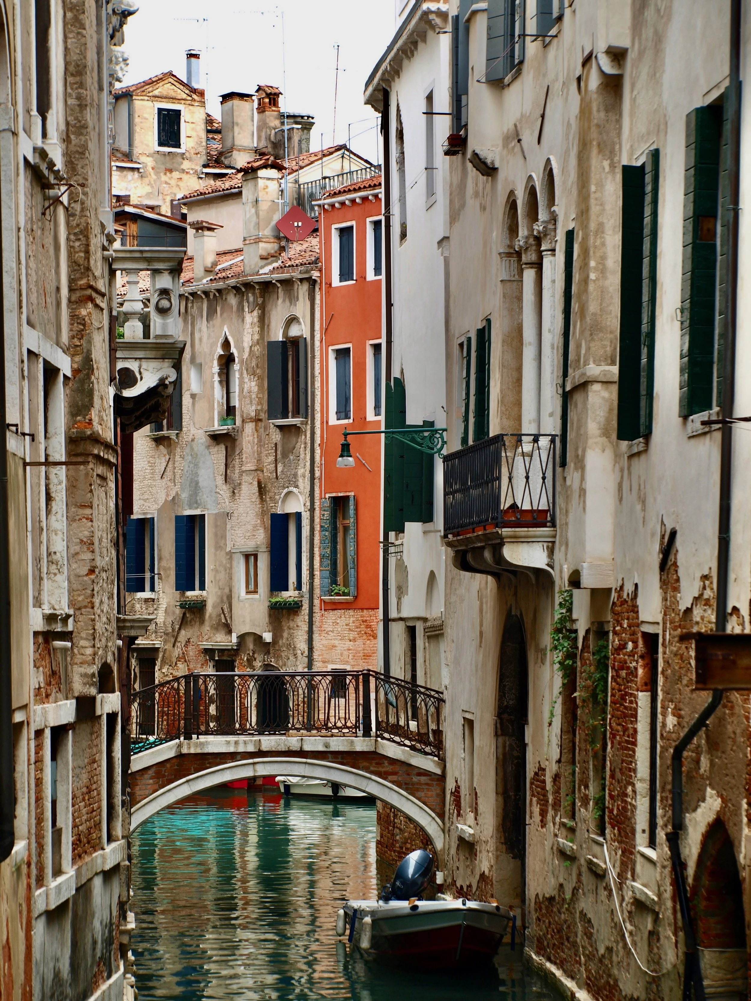 Une rue étroite avec des bâtiments anciens et une petite canalisation d'eau avec un bateau à moteur. Un pont en pierre en arc sur l'eau.