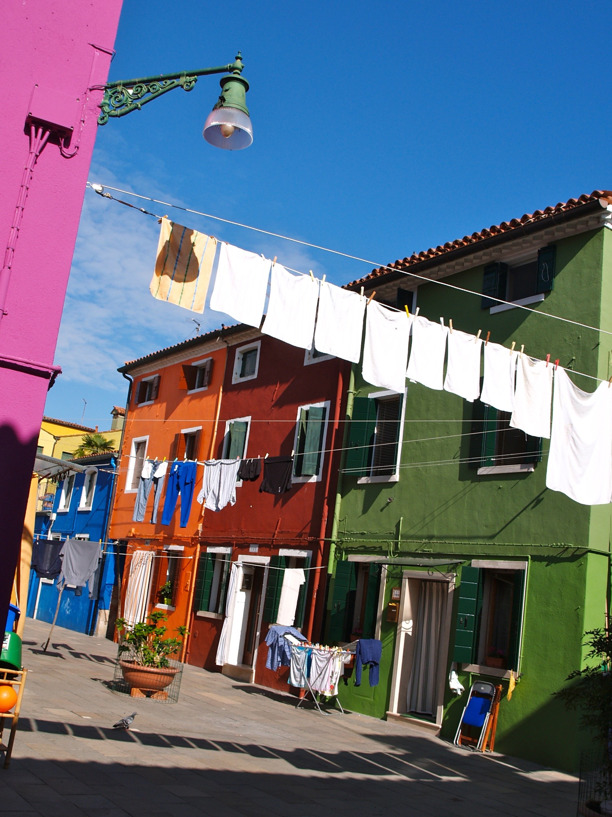 Colorful buildings with laundry hanging on lines outside on a sunny day, featuring a pink, orange, and green facades in a vibrant neighborhood.