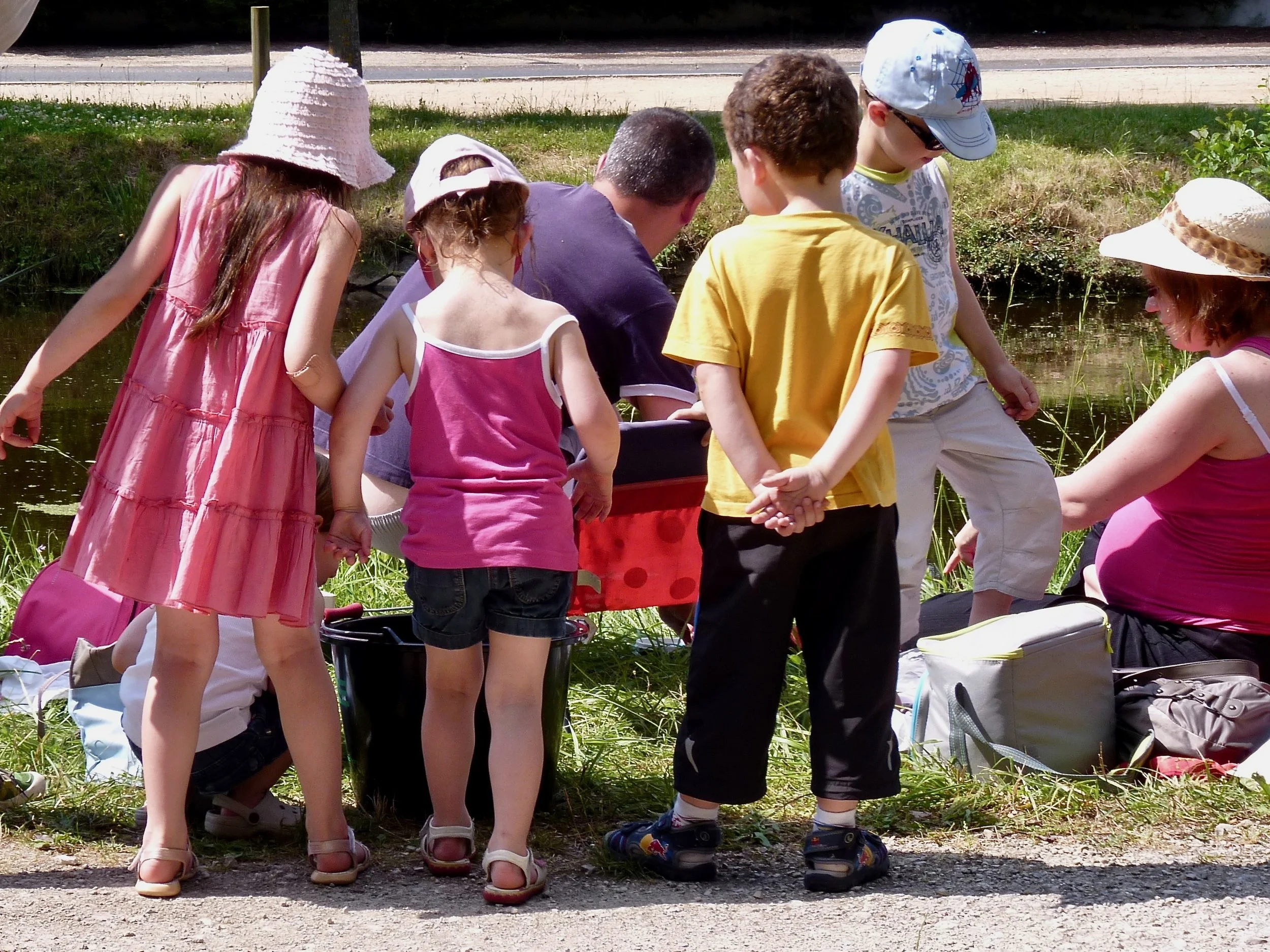 Groupe d'enfants, certains portant des chapeaux, qui regardent quelque chose dans l'eau en extérieur.