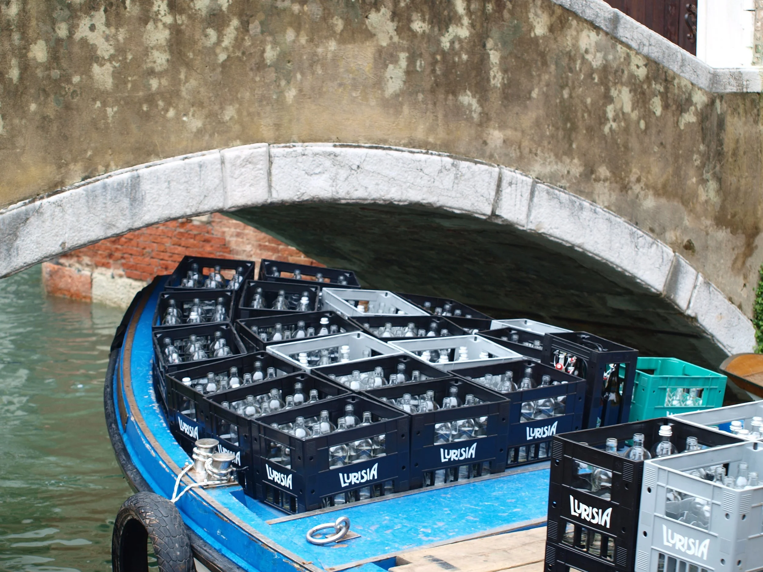 Un bateau de livraison de bouteilles d'eau naviguant sous un pont en pierre dans un canal.
