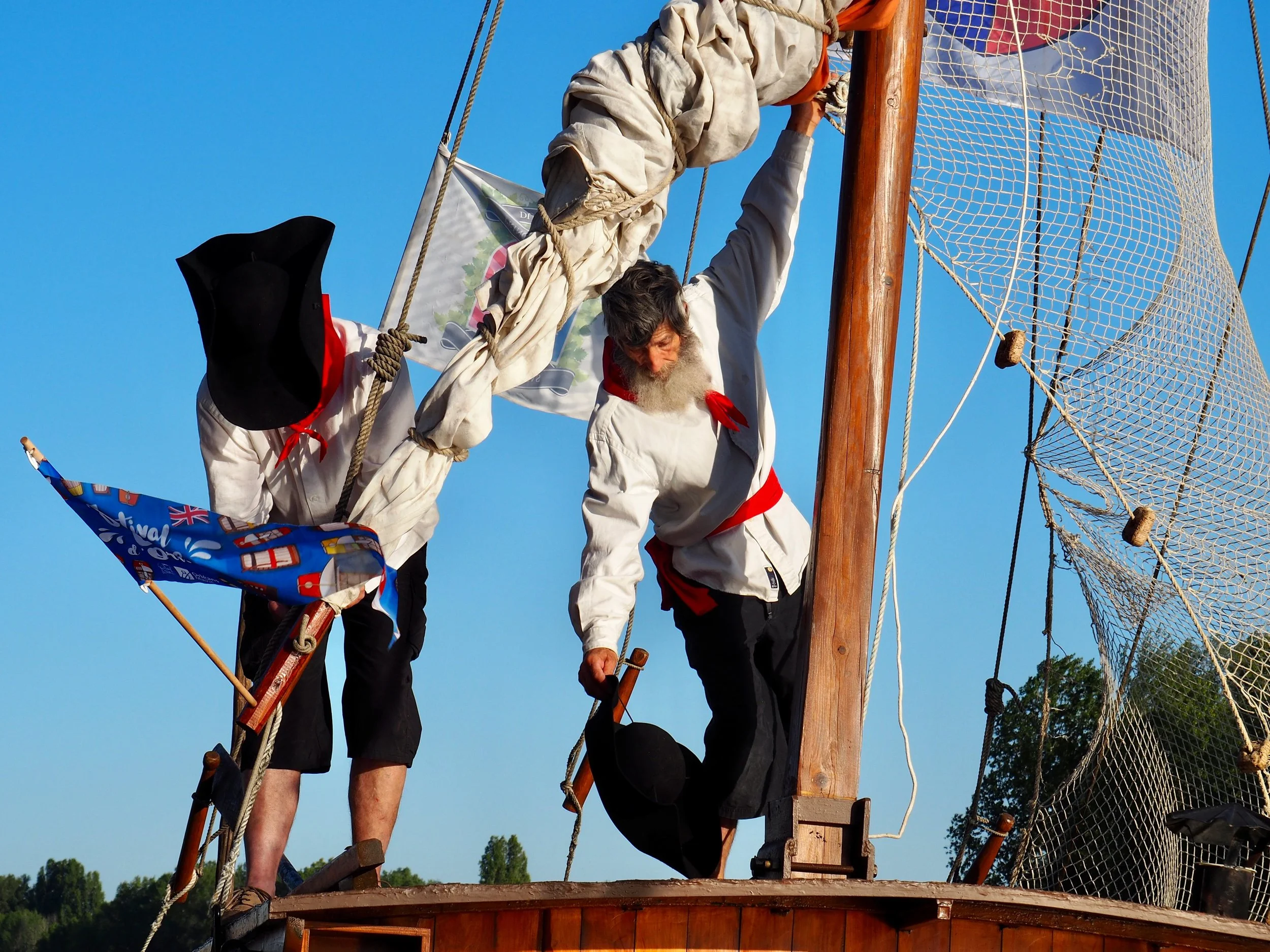 Des personnes en uniforme blanc, quelques-uns portant des bandanas rouges, en train de grimper ou d'équilibrer sur une structure en bois et en corde, lors d'une activité extérieure sur un ciel clair.