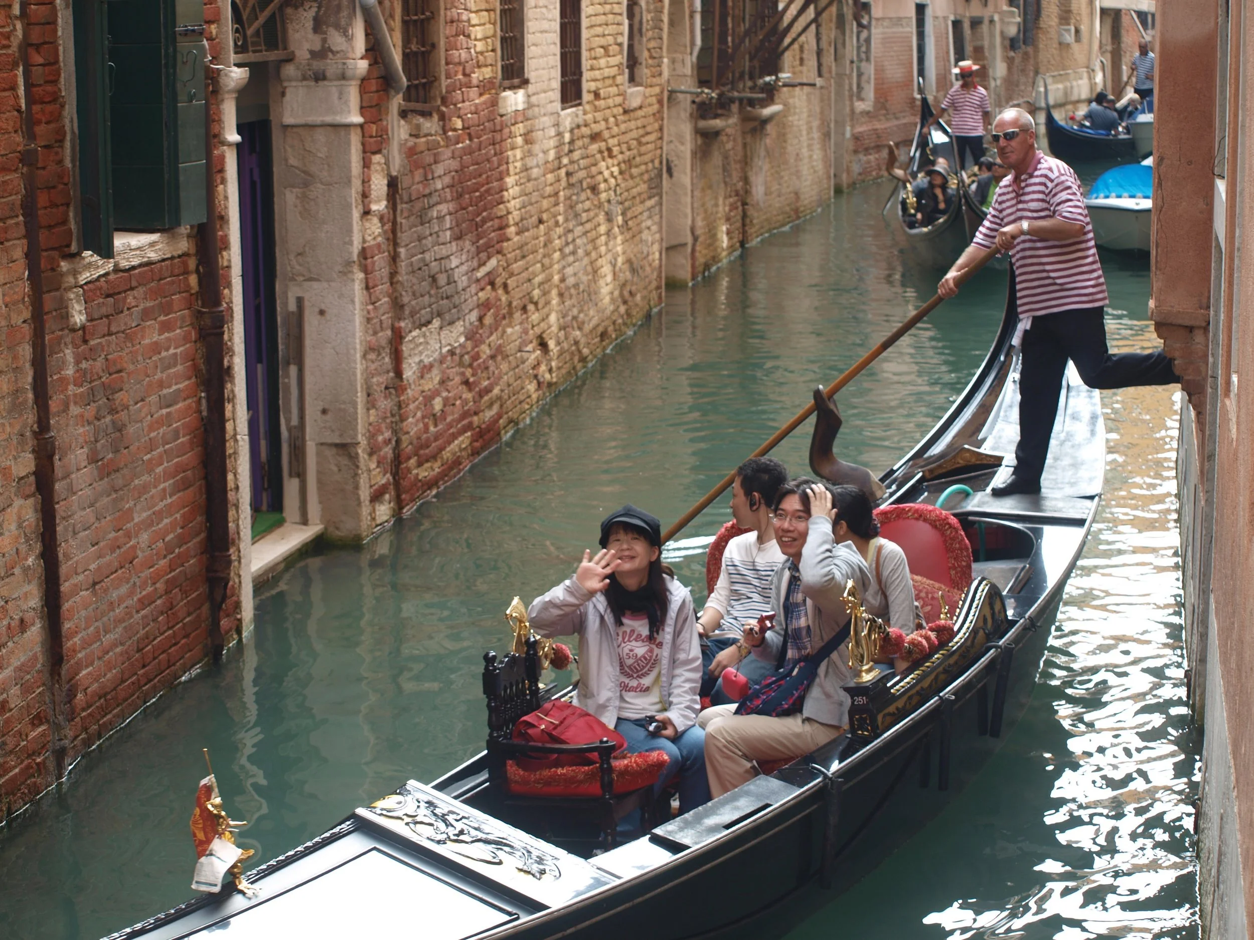 Gondoleurs glissant une gondole à travers un canal étroit de Venise avec des bâtiments en briques anciennes sur les côtés.