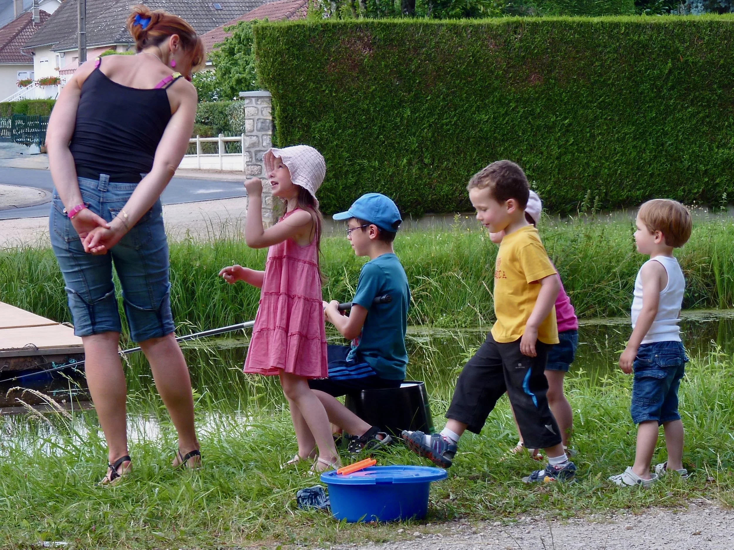 Groupe d'enfants et une femme près d'un étang dans un jardin, jouant avec des jouets.
