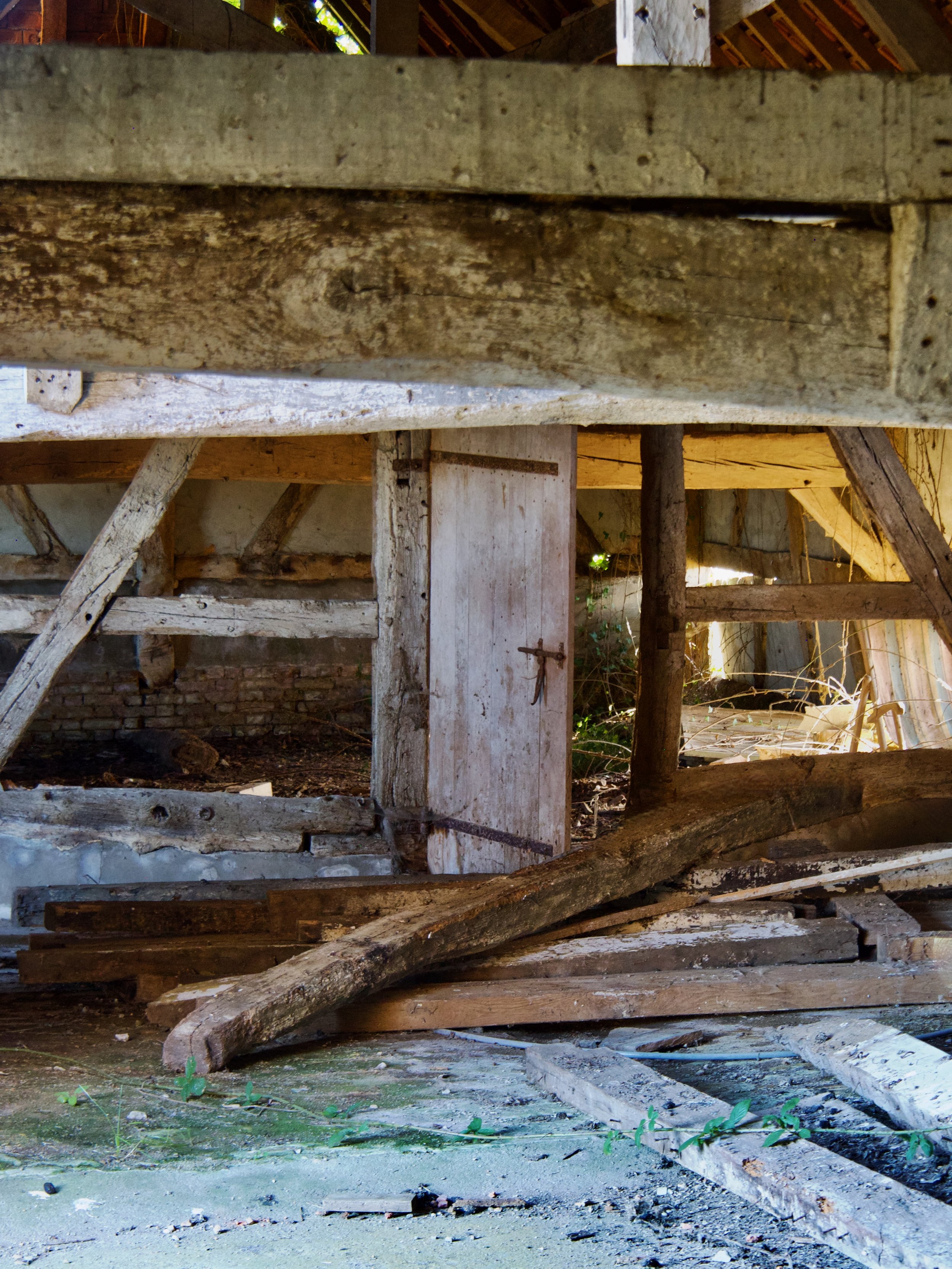 Structure en bois en ruine avec des poutres cassées et des débris au sol, probablement l'intérieur d'une vieille bâtisse ou grange abandonnée.