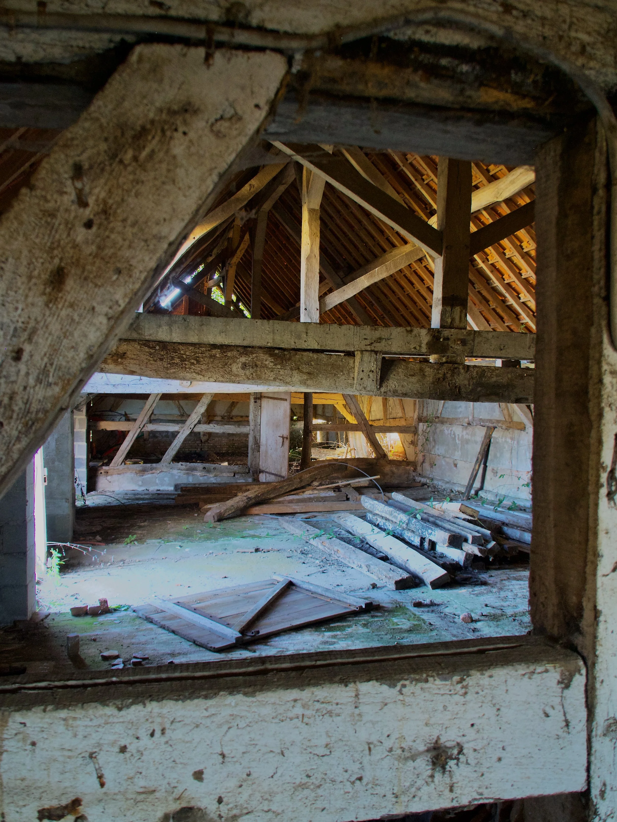 Vieux bâtiment en rénovation avec des structures en bois, débris sur le sol et un toit en tuiles en cours de réparation.