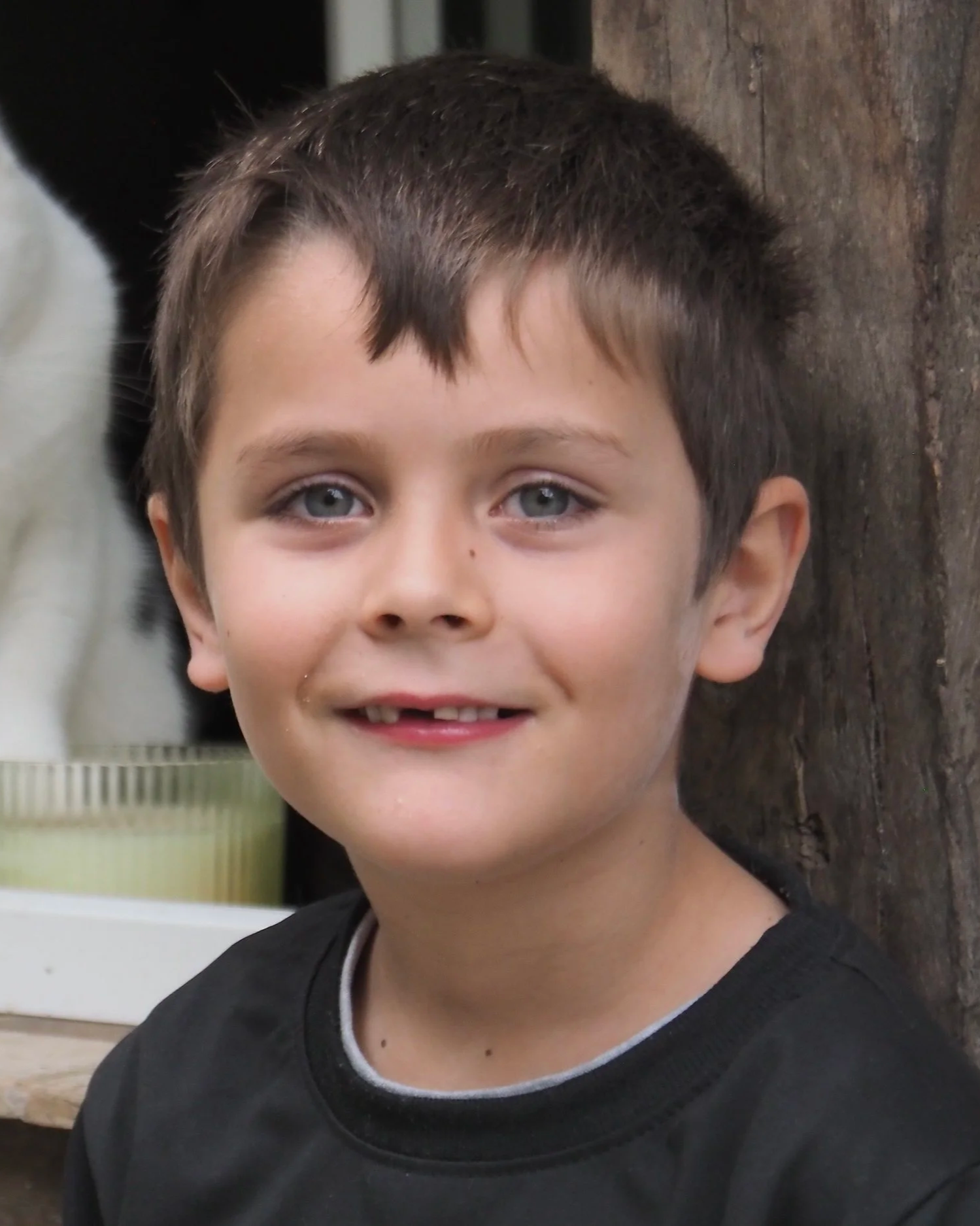 Portrait d'un jeune garçon avec des cheveux courts et bruns, portant un sweat noir, souriant légèrement, avec un fond en bois et un mur blanc.