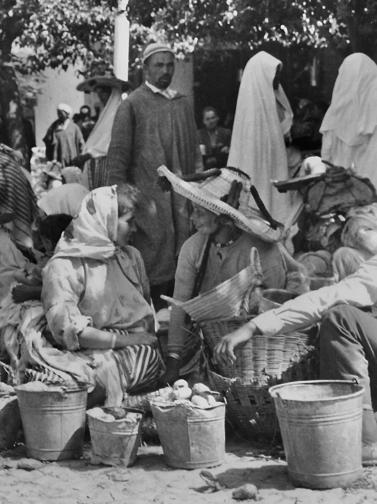 Marché avec plusieurs vendeurs et acheteurs, femmes avec foulards et un homme avec un chapeau, étals avec paniers et seaux