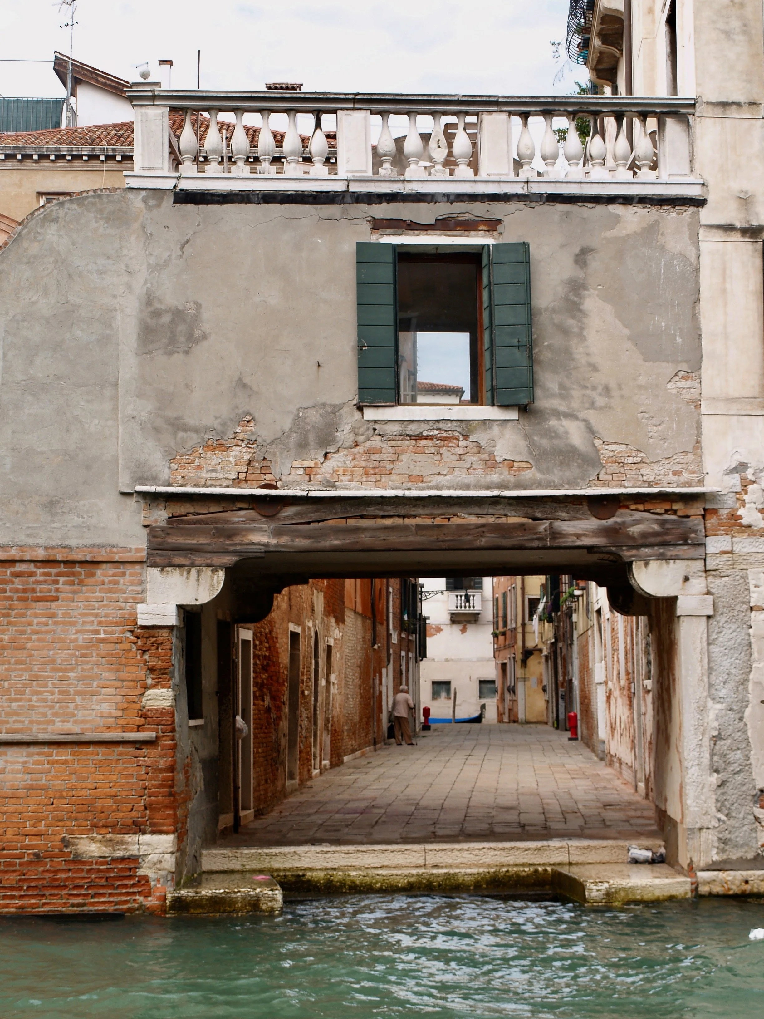 Un canal avec de l'eau, entouré de bâtiments en pierre et en brique anciennes, avec une passerelle en pierre et des arches en dessous, typique de Venise, en Italie.