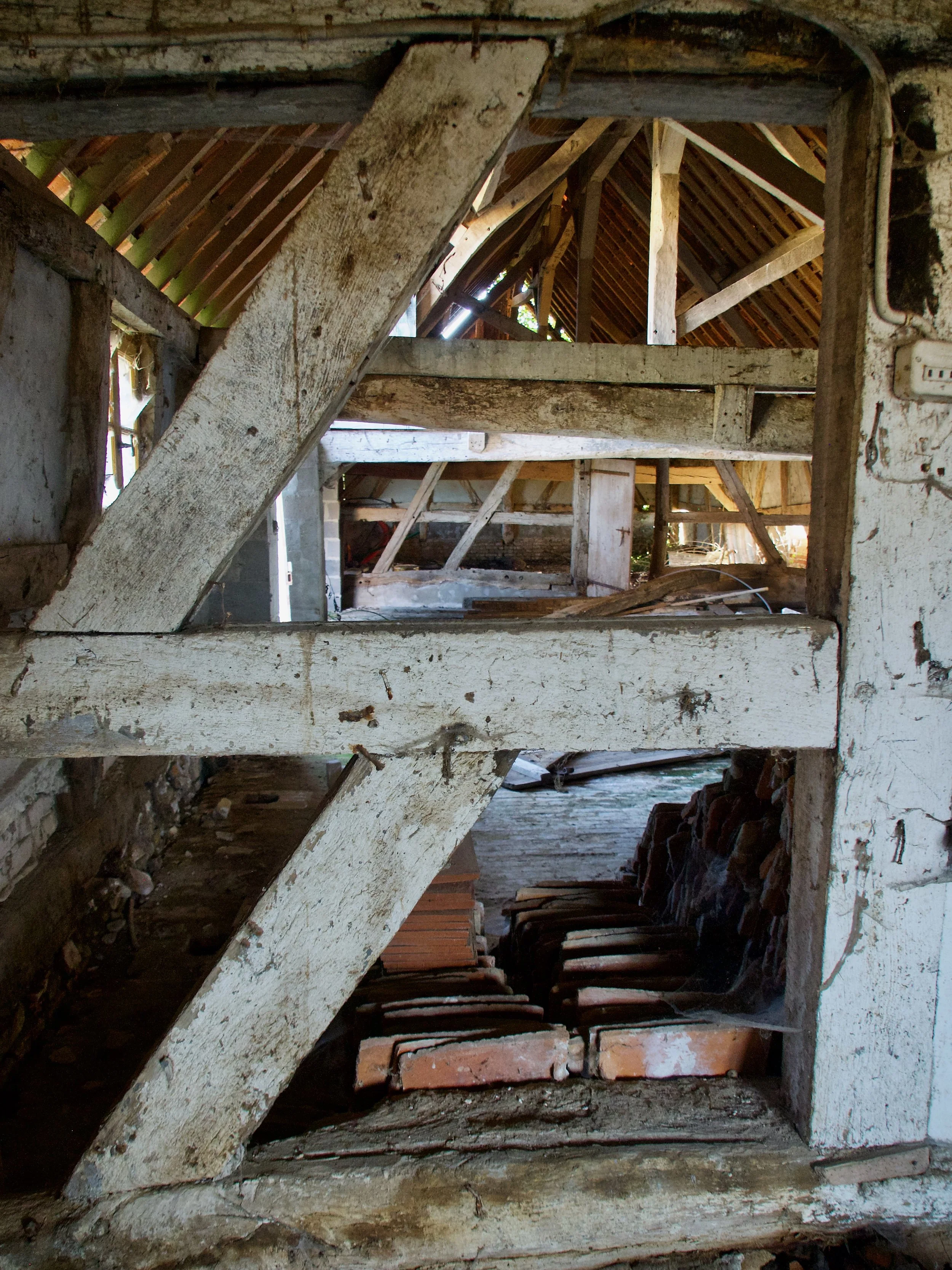 L'intérieur d'une vieille grange ou ferme en bois avec des sections de murs partiellement abattus et un toit en pente en bois, visible à travers une ouverture dans le mur.