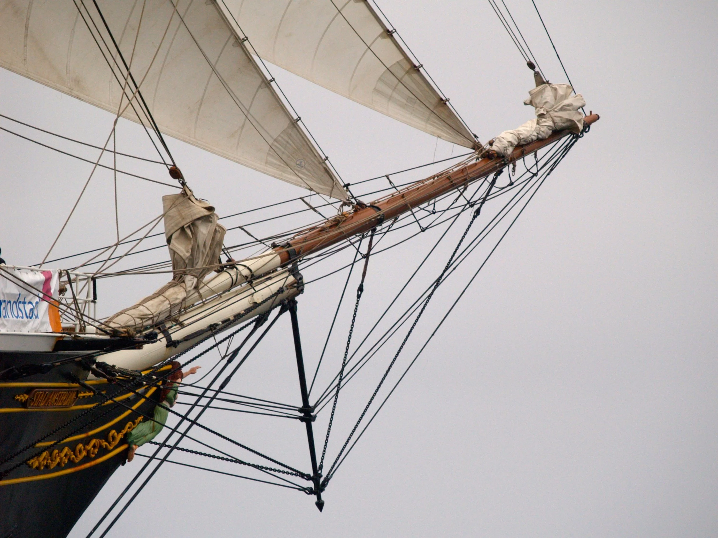 Un mât de voilier avec des cordages et des voiles déployés contre un ciel gris.