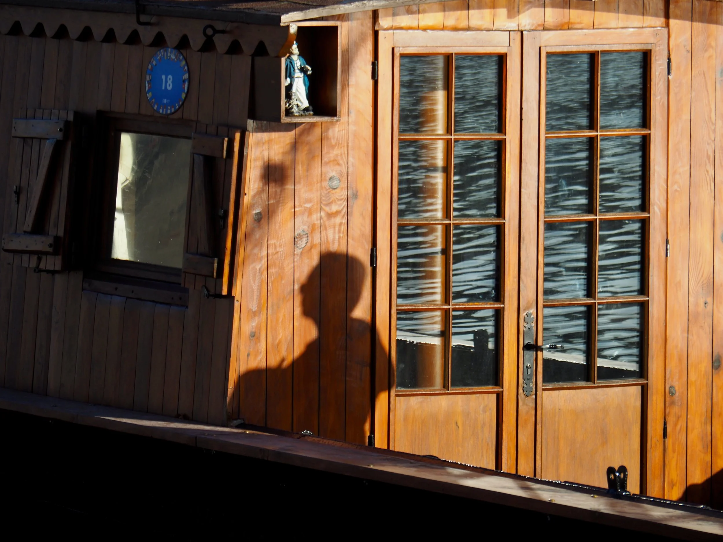 Une cabine en bois avec des fenêtres en verre et une horloge bleue. Un petit figurine en costume traditionnel est placée dans une niche au-dessus de la porte.