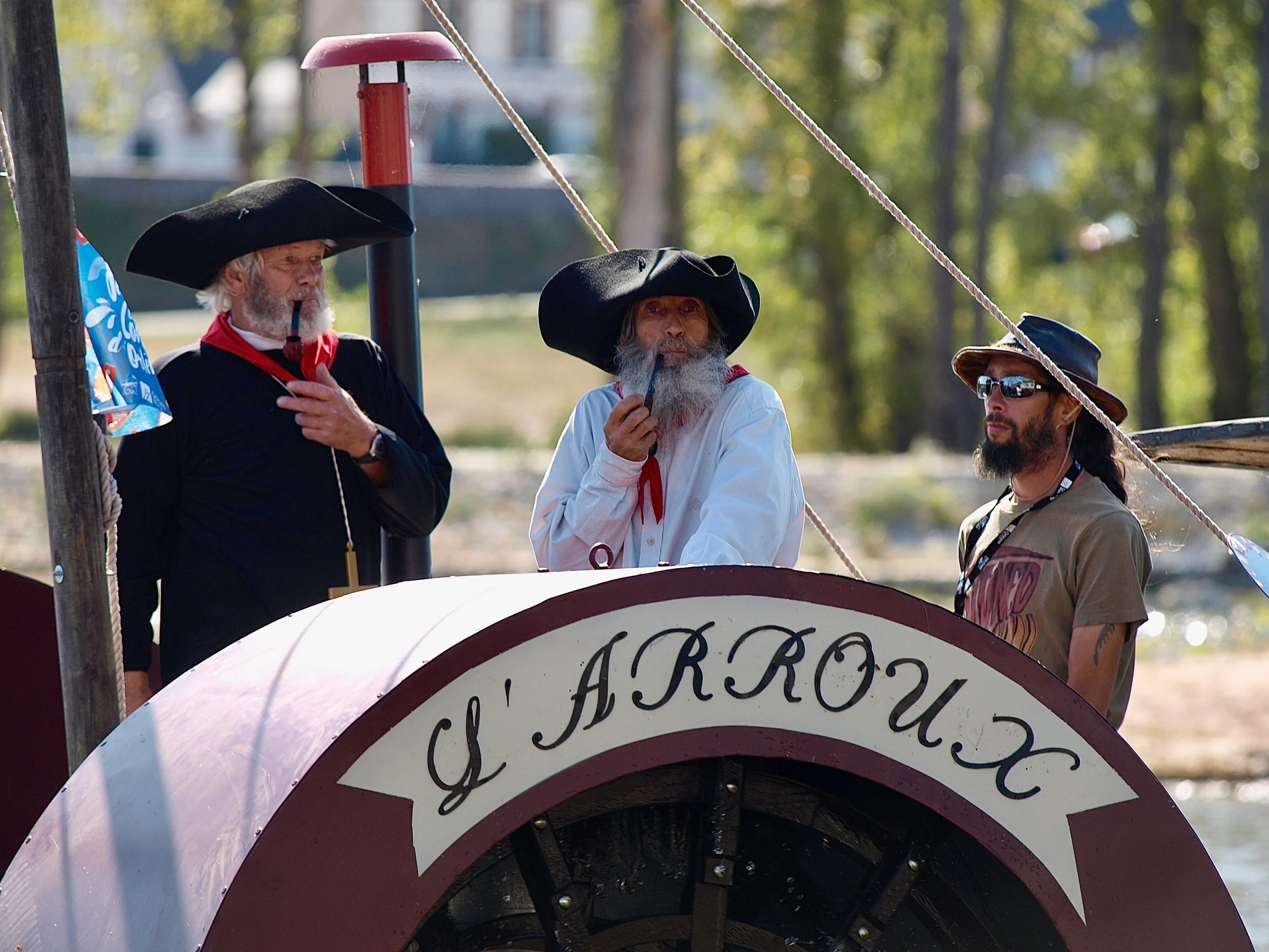Trois hommes en costumes et chapeaux de pirates, tenant des pipes, sont debout derrière une structure en plastique avec un panneau écrit 'AEROS'.