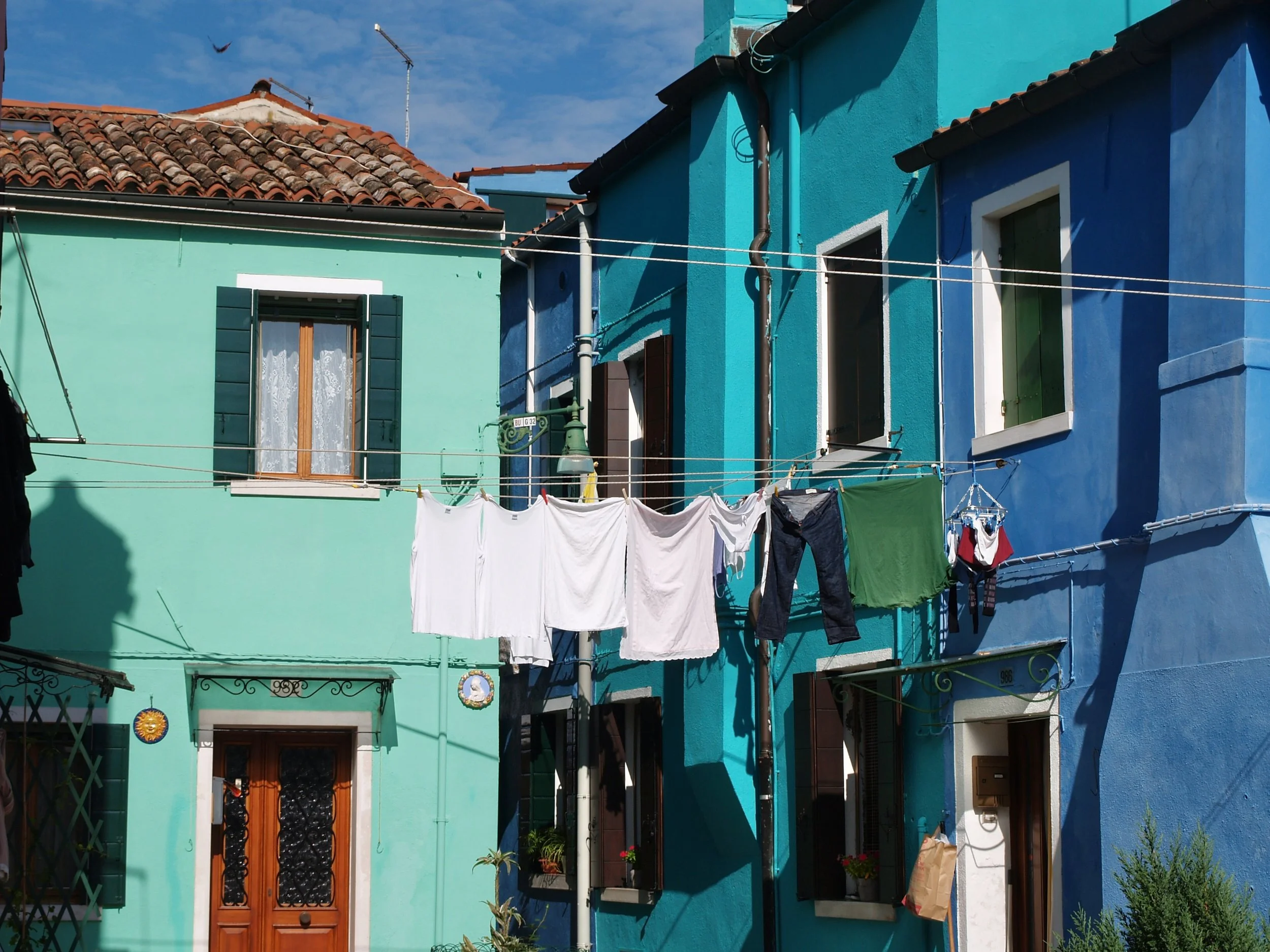 Des maisons colorées en bleu et vert avec des fenêtres, des volets et des lignes à linge suspendues devant elles.