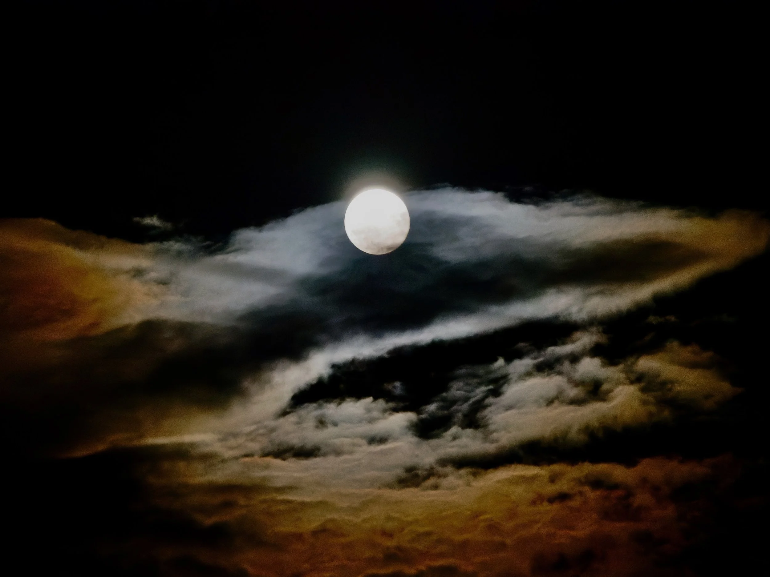 Une lune pleine dans un ciel nuageux avec des nuages sombres et quelques éclaircies.