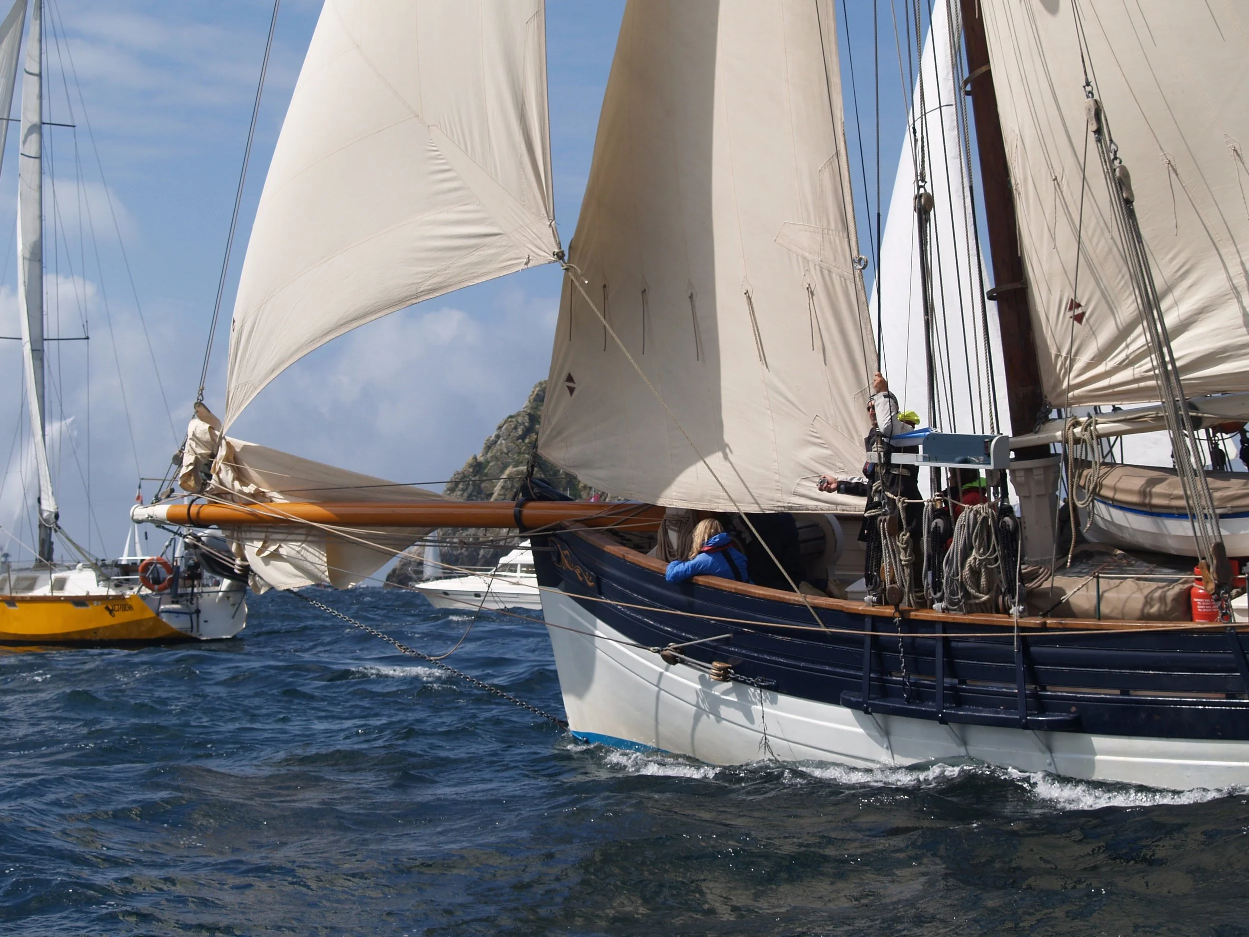 Voilier avec ses voiles déployées naviguant sur la mer, ciel partiellement nuageux en arrière-plan.