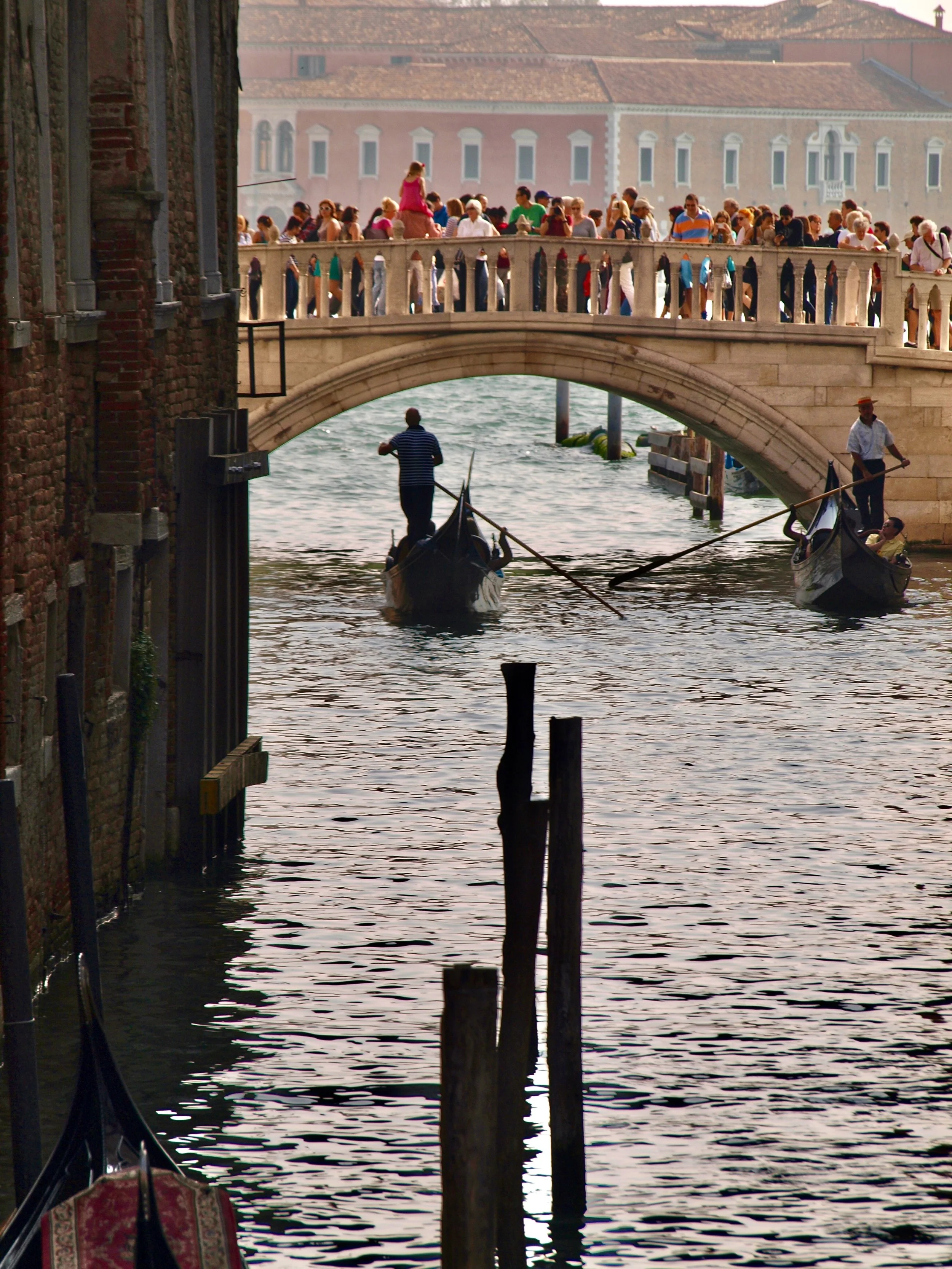 Gondolier naviguant une gondole dans la Venise historique, avec un pont et un grand nombre de passagers sur le pont dans un paysage urbain typique de Venise, Italie.