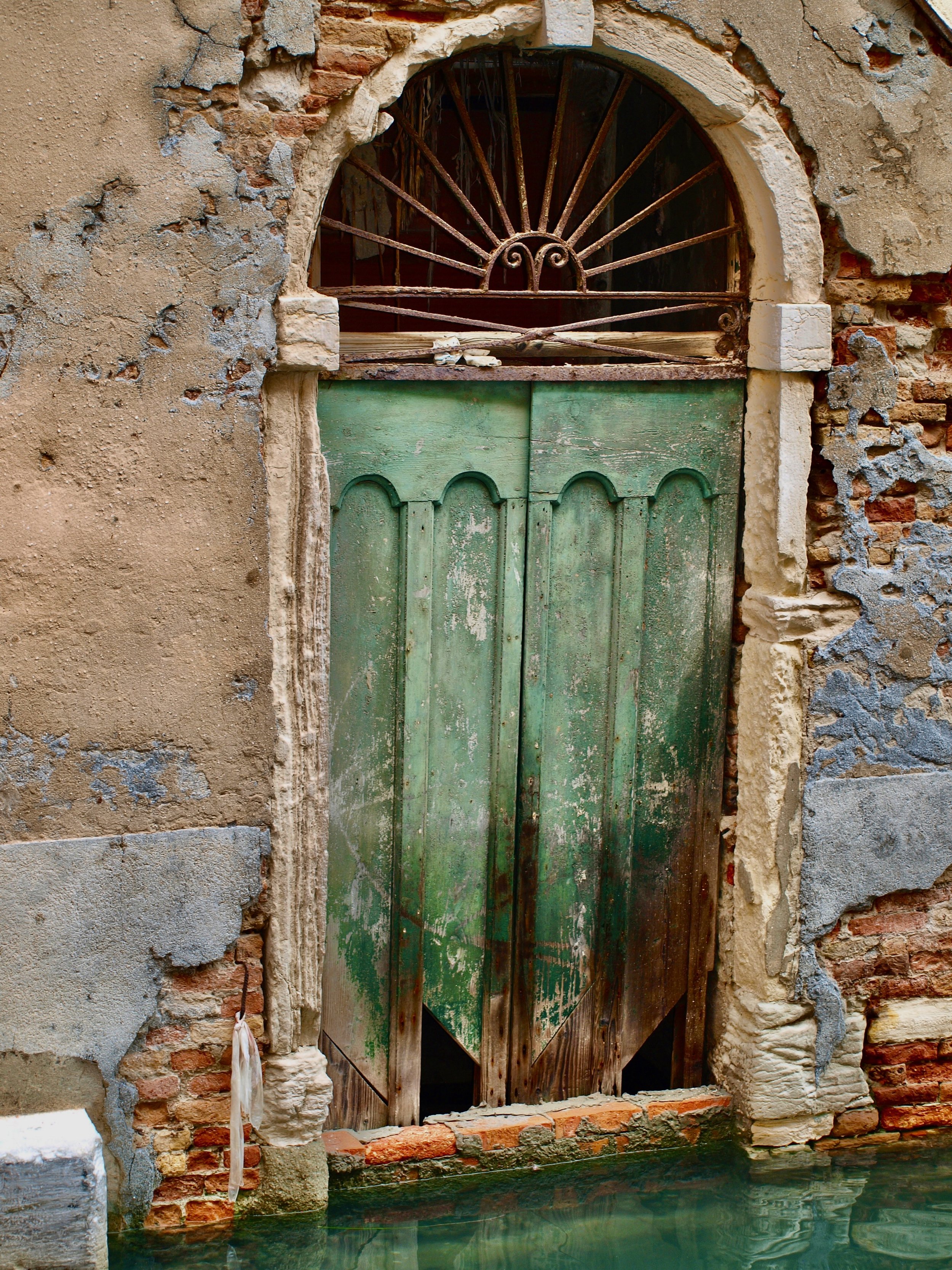 Une vieille porte en bois vert, encadrée par un mur en briques et pierres, débouche sur une étendue d'eau stagnant à ses pieds.