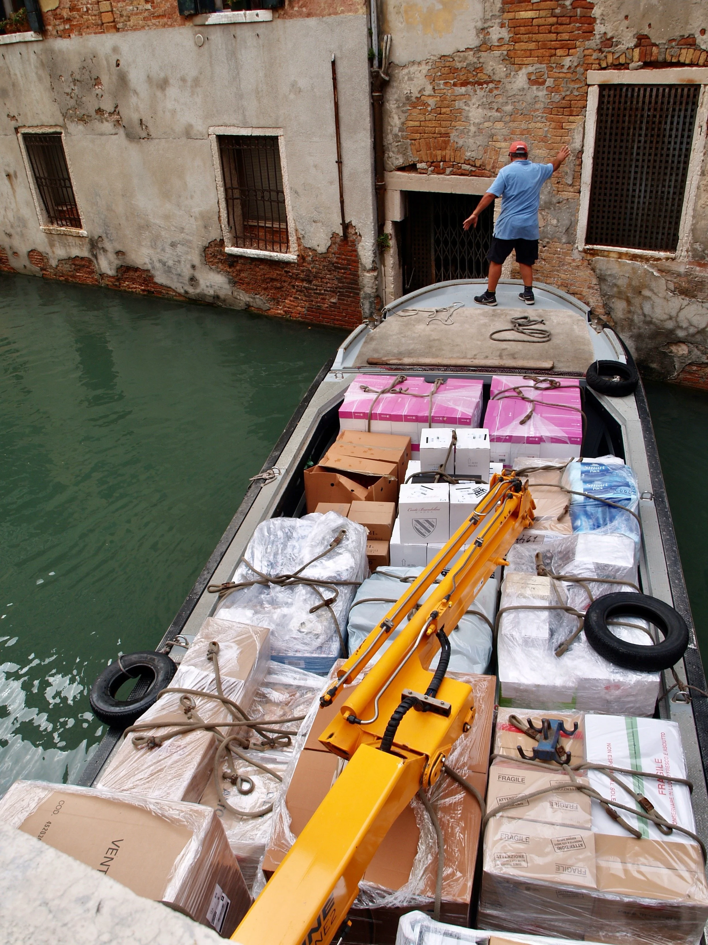 Une personne debout sur un ponton regardant une maison aux murs en brique et en béton, avec des fenêtres grillagées, sur un canal.