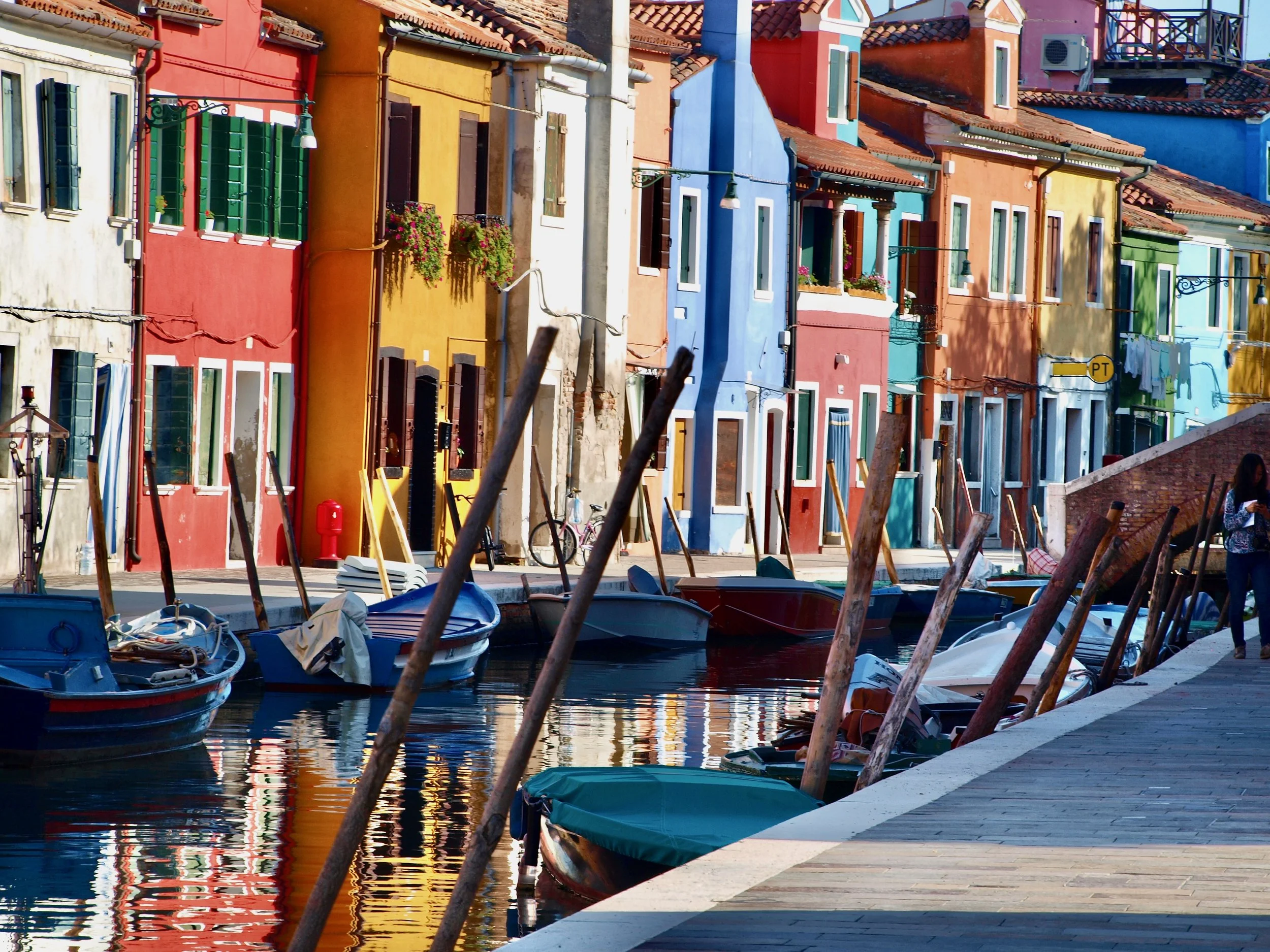 Maisons colorées le long d'un canal avec des petits bateaux à voile amarrés au bord de l'eau, dans un port.
