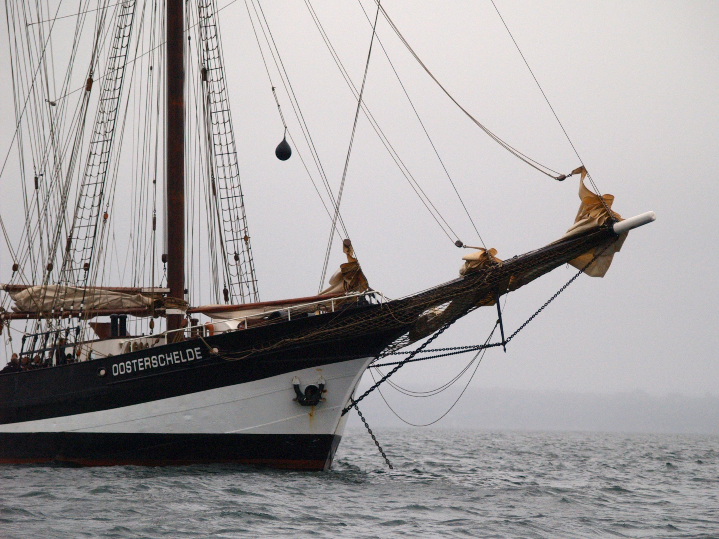 Un grand voilier avec de nombreux cordages et voiles, nommé "Oosterschelde", naviguant en mer par temps nuageux.