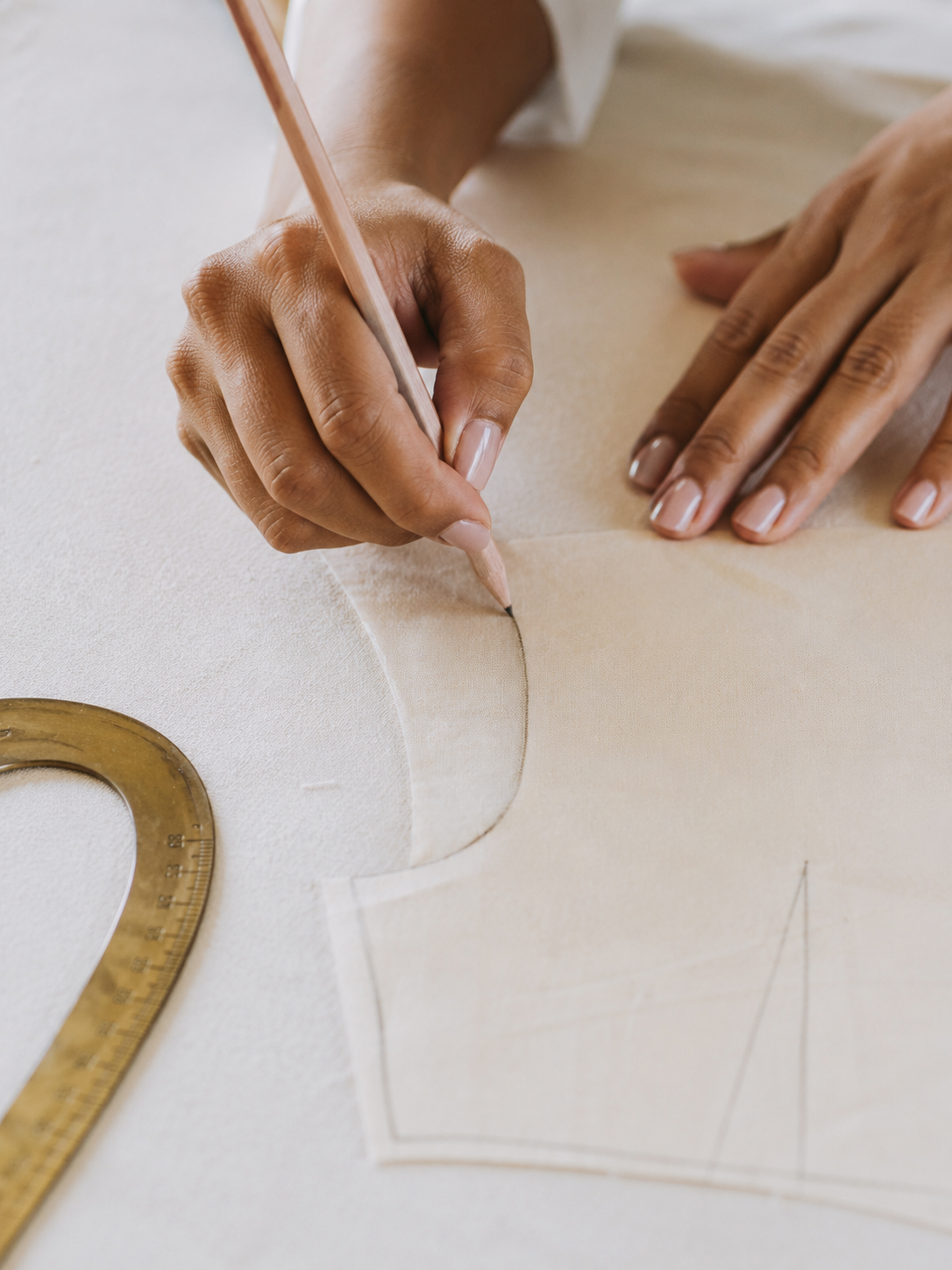 Une personne trace un patron en tissu pour la couture, avec une règle en bois, sur une surface claire.