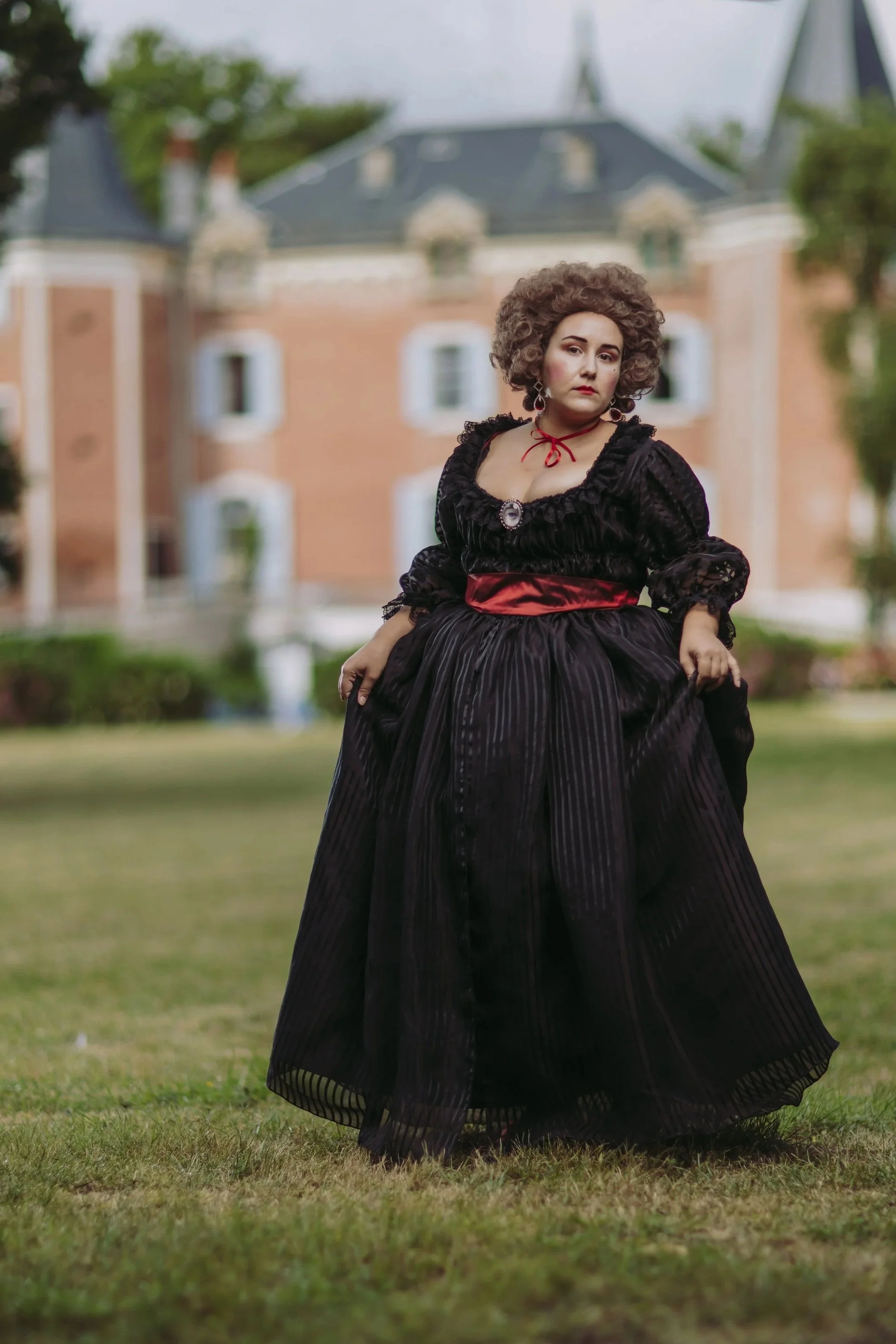 Une femme habillée avec une chemise à la reine en gaze rayée noire 18ème siècle costume historique devant un château rococo