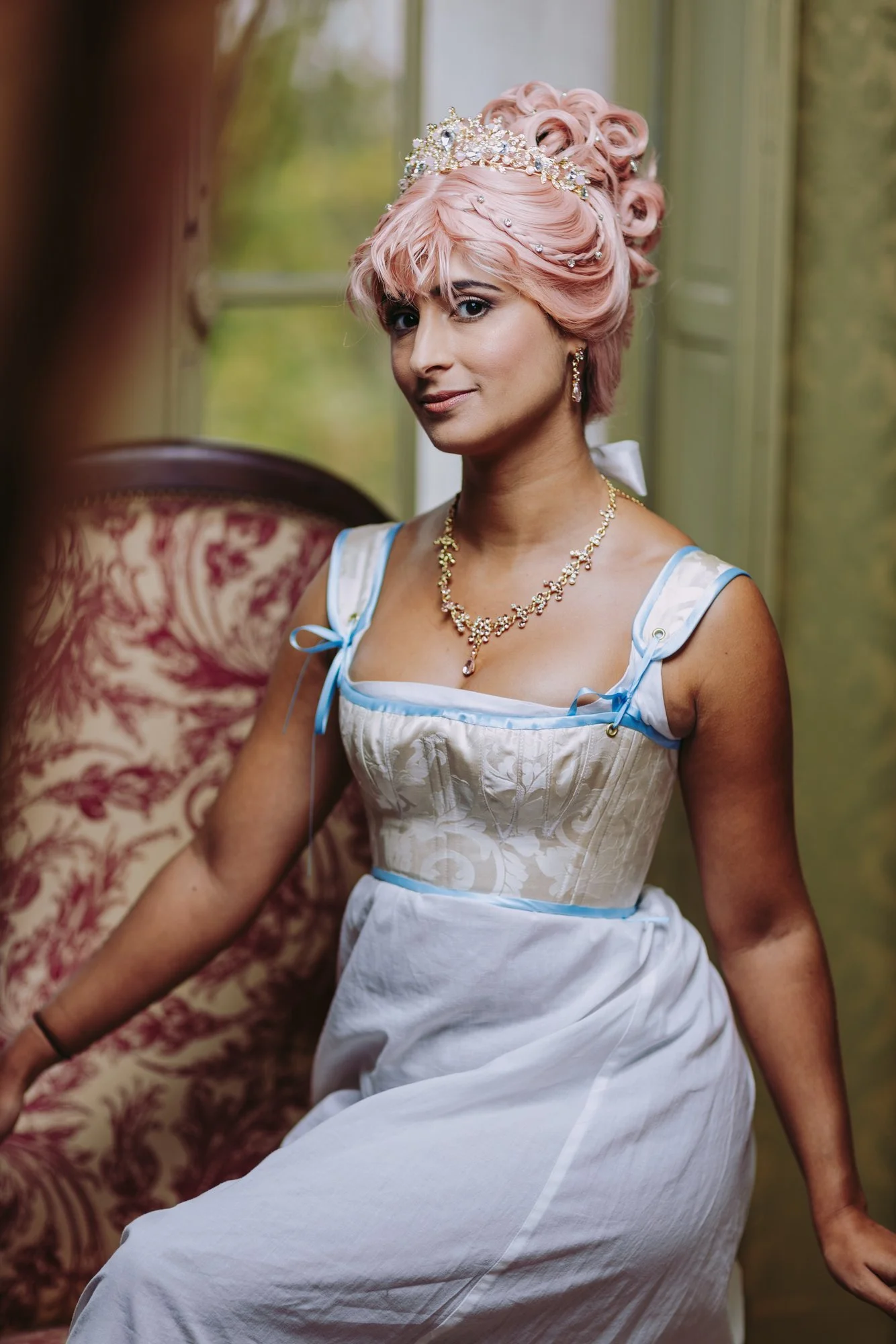 Une femme portant des sous vêtement historique premier empire et une coiffure inspirée de brigerton : une chemise de corps et un corselet structurant à goussets assise dans la chambre d'un château