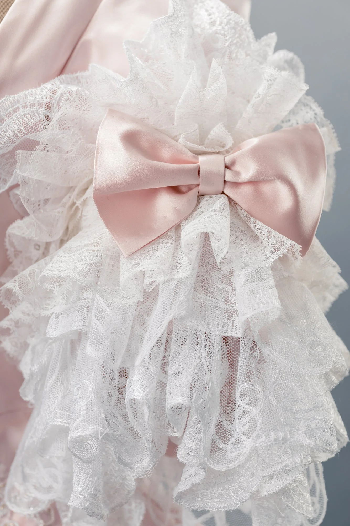 Détail d'une décoration avec un grand nœud de satin rose clair, entouré de dentelle blanche en bandeaux et ruffles.