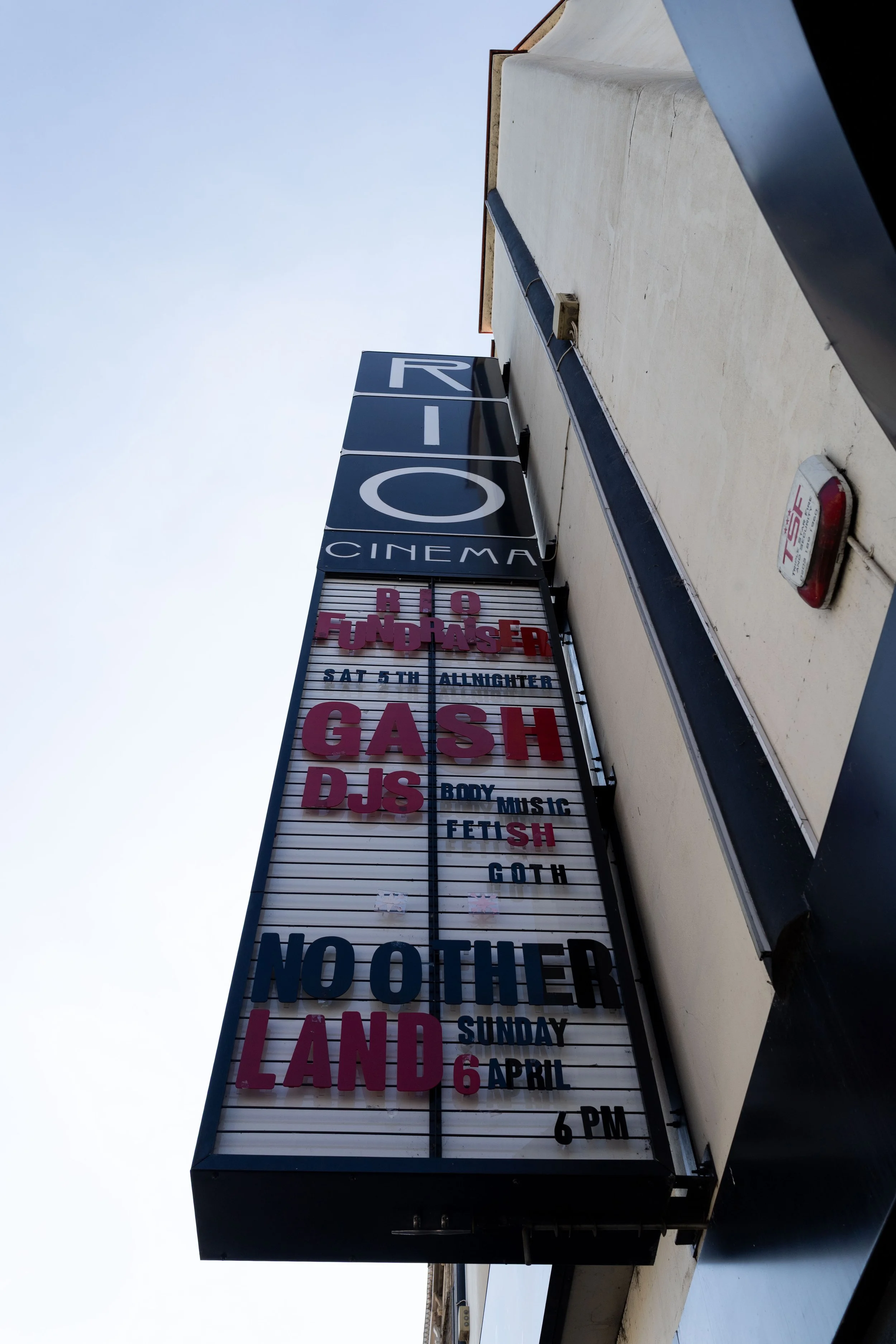 A vertical marquee sign outside a building displaying upcoming events and dates, located under a blue sky.