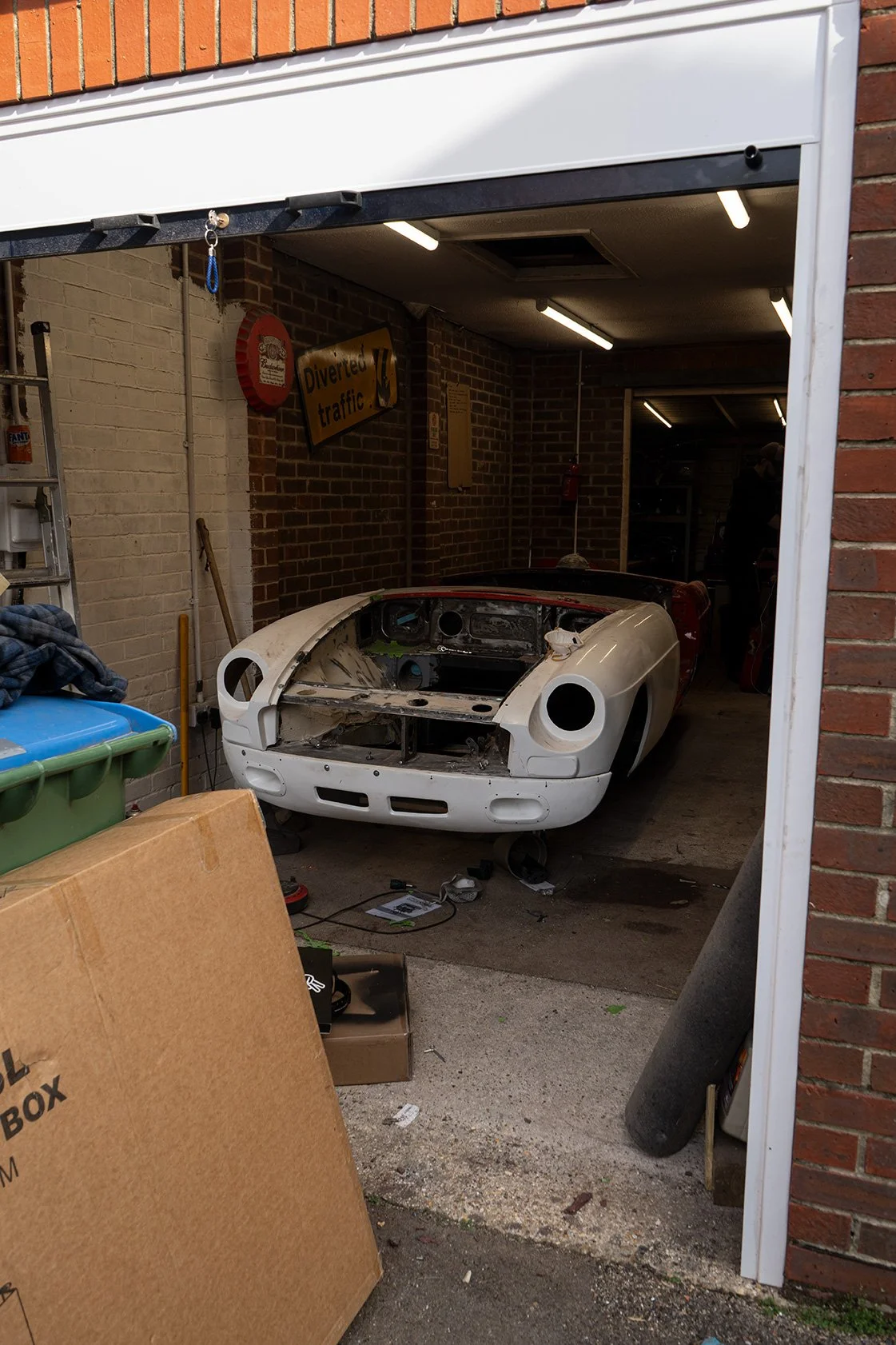 A garage with a partially assembled white vintage sports car, surrounded by tools and car parts.