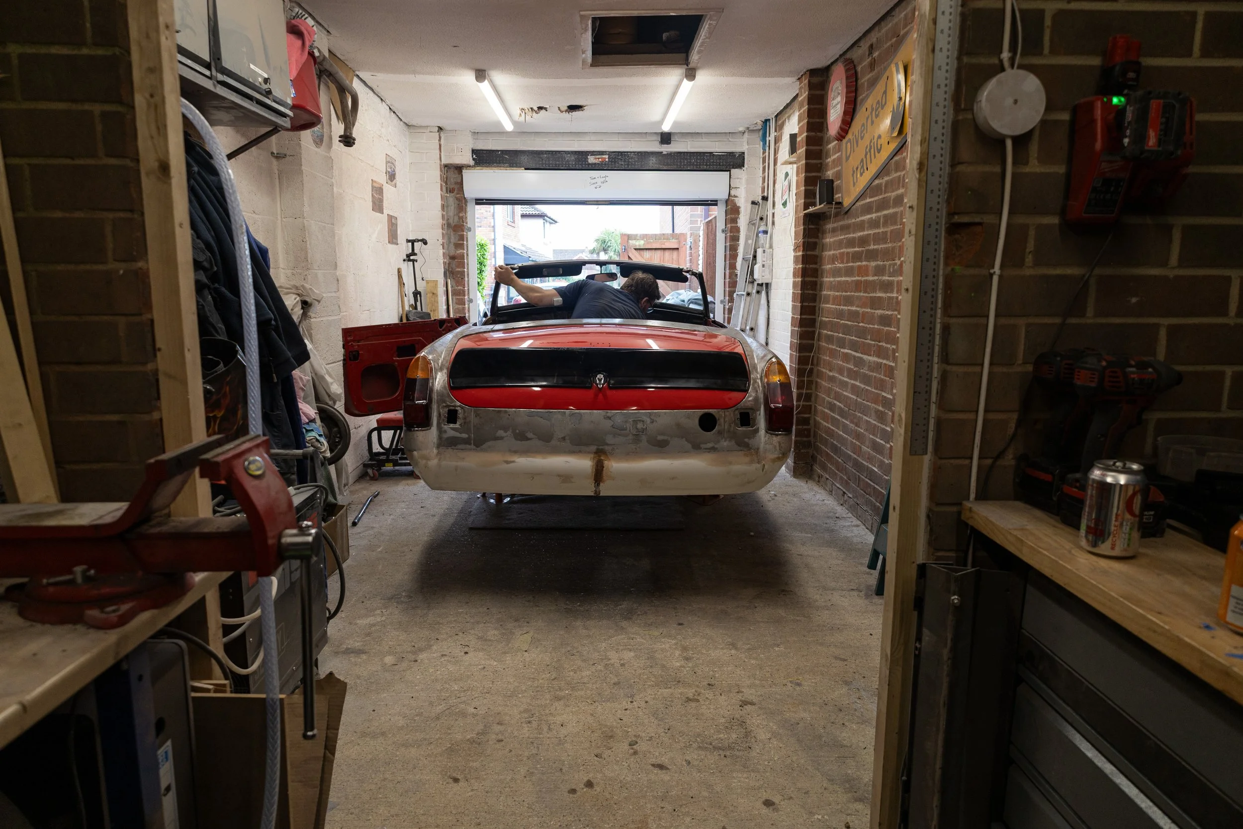 A person working on restoring a car in a garage with shelves, tools, and a sign that reads 'Diverter traffic'.