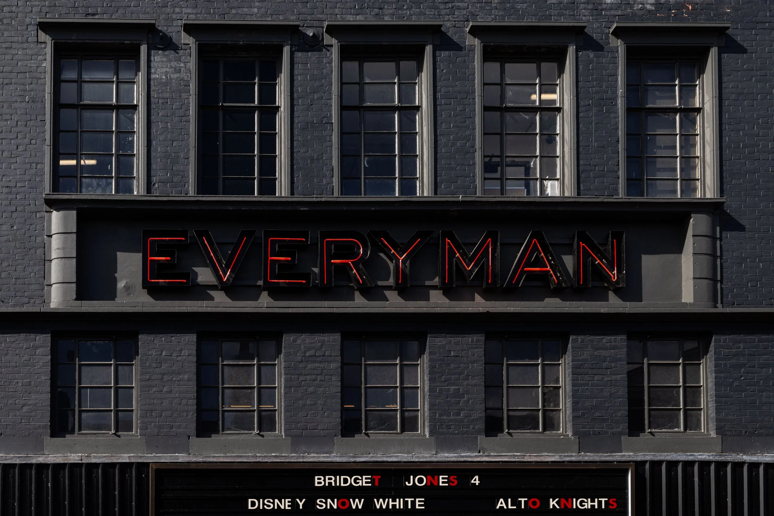 A dark gray brick building with four tall windows on the top floor. Below the windows is a neon sign that reads 'EVERYMAN'. Underneath, a marquee shows the text: 'BRIDGET JONES 4 DISNEY SNOW WHITE ALTO KNIGHTS'.