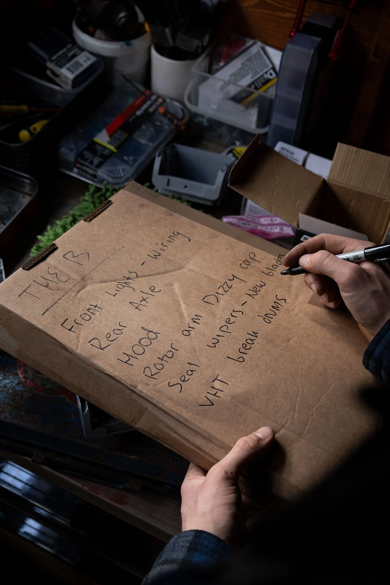 Person holding a brown paper bag with handwritten meal instructions, surrounded by storage bins and tools in a workshop setting.