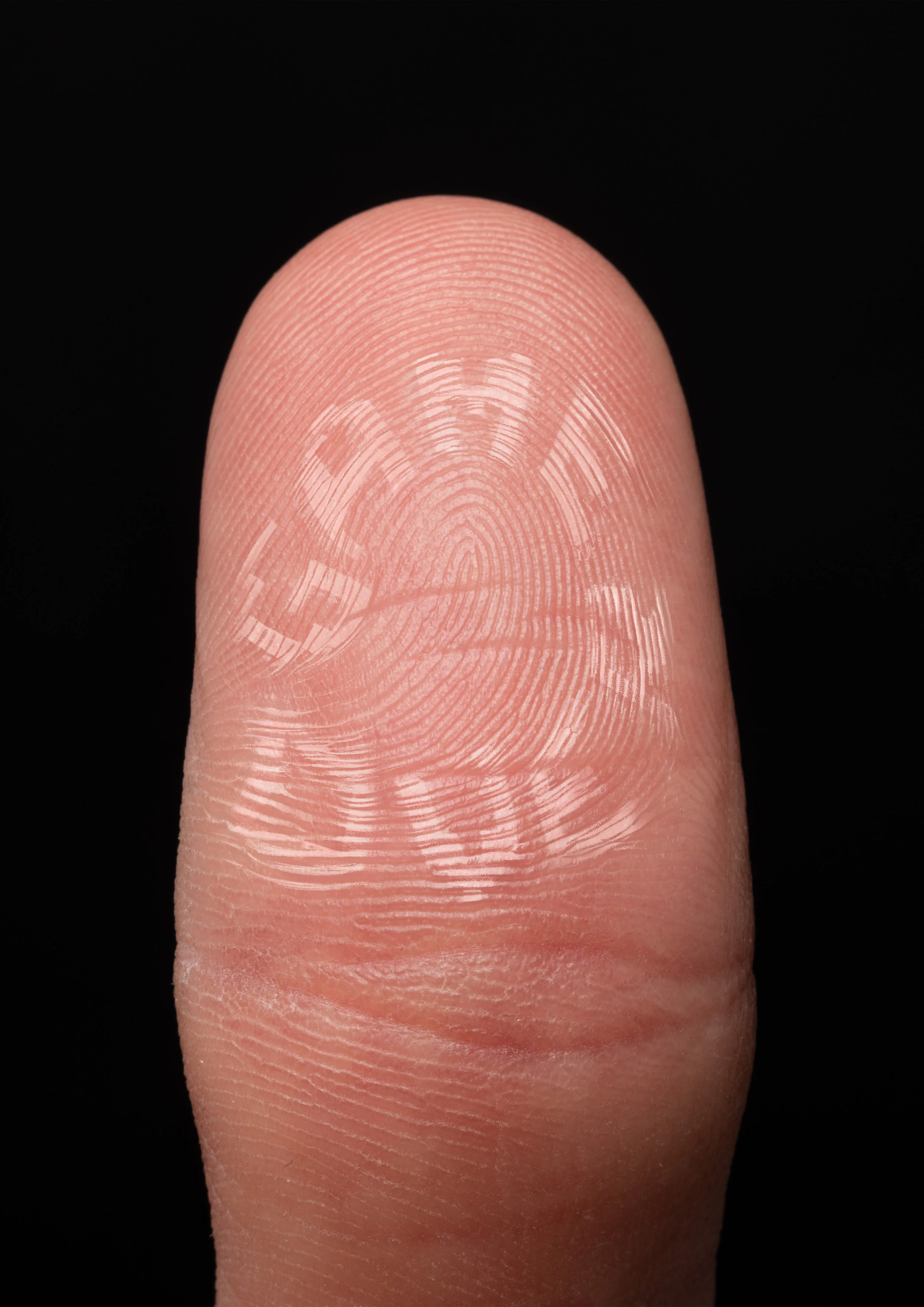 Close-up of a human fingerprint on a fingertip against a black background.
