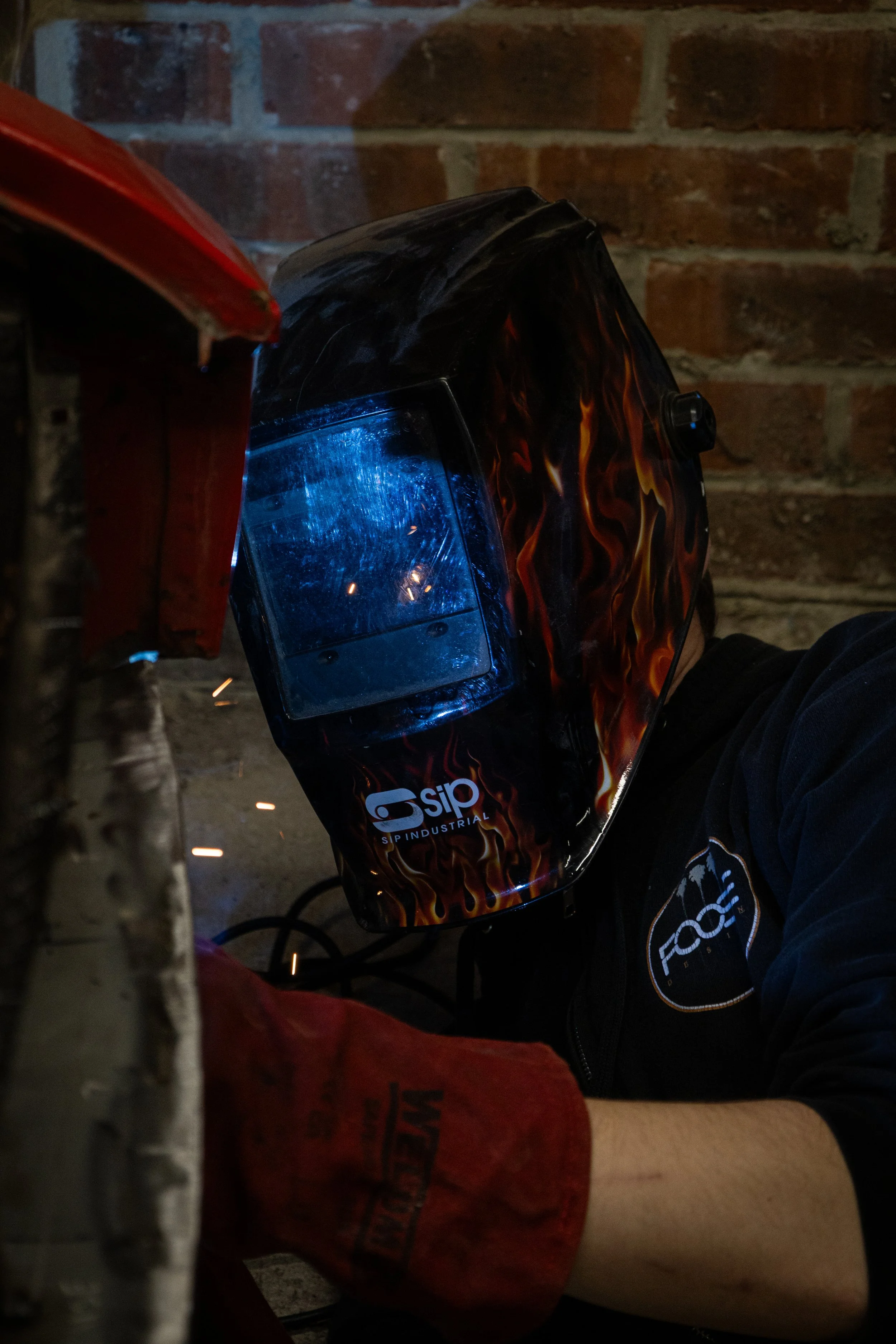 A person welding with a welding helmet and protective gear in a workshop, sparks flying from the welding process.