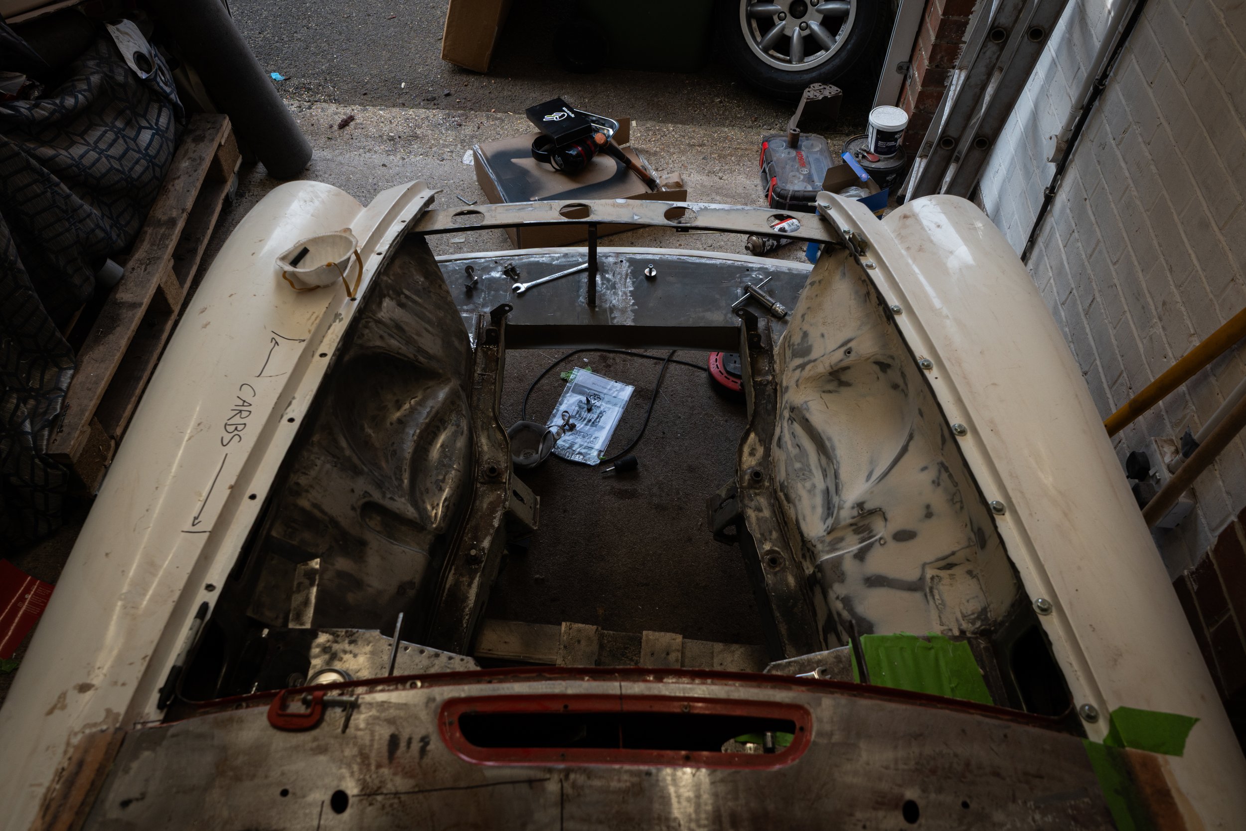 Partial view of a vintage car body shell in the process of restoration, situated inside a garage with tools and car parts around.