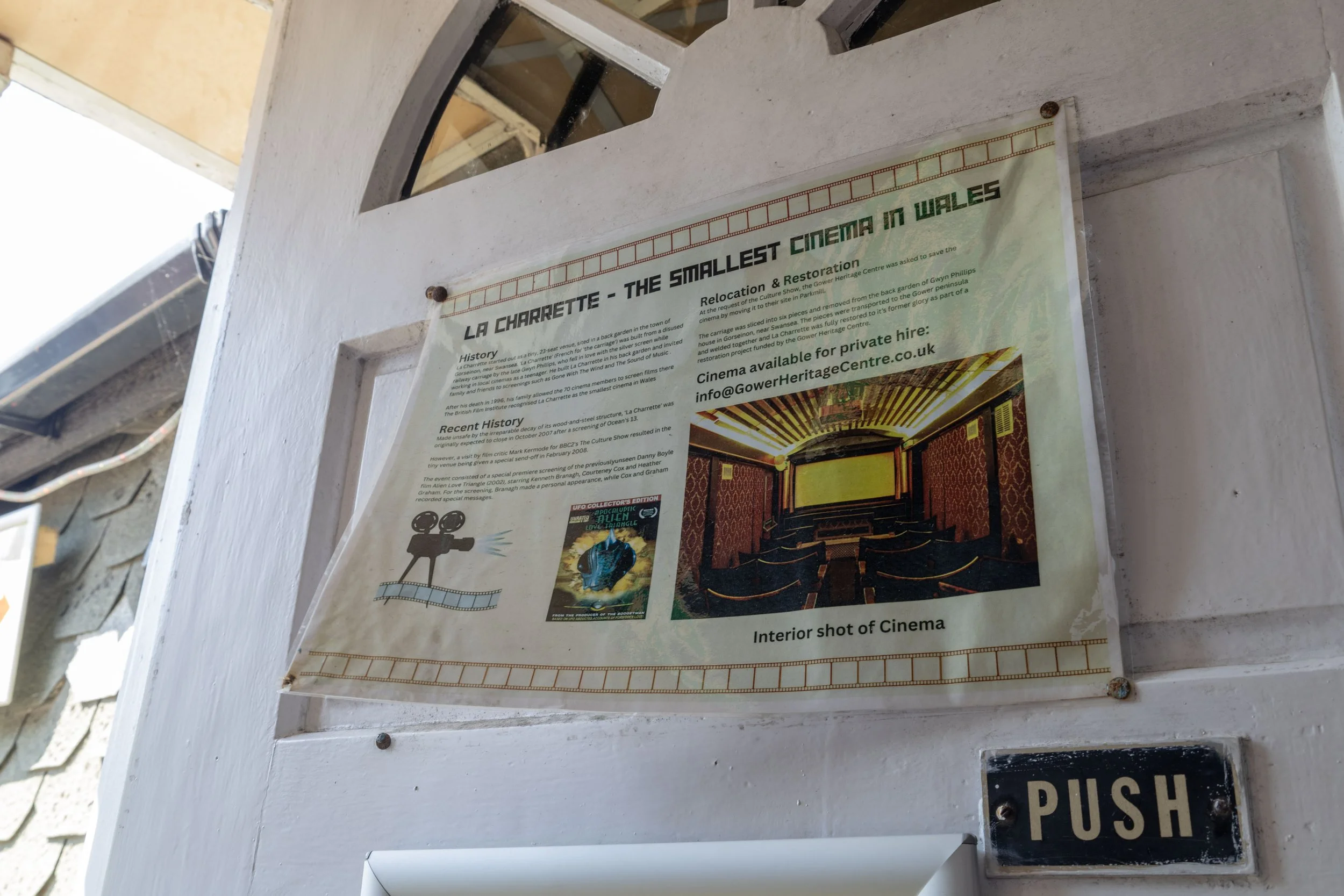 Sign about La Charrette, the smallest cinema in Wales, describing its history and restoration, with a photograph of the cinema interior showing red patterned walls, yellow curtains, and theater seats.