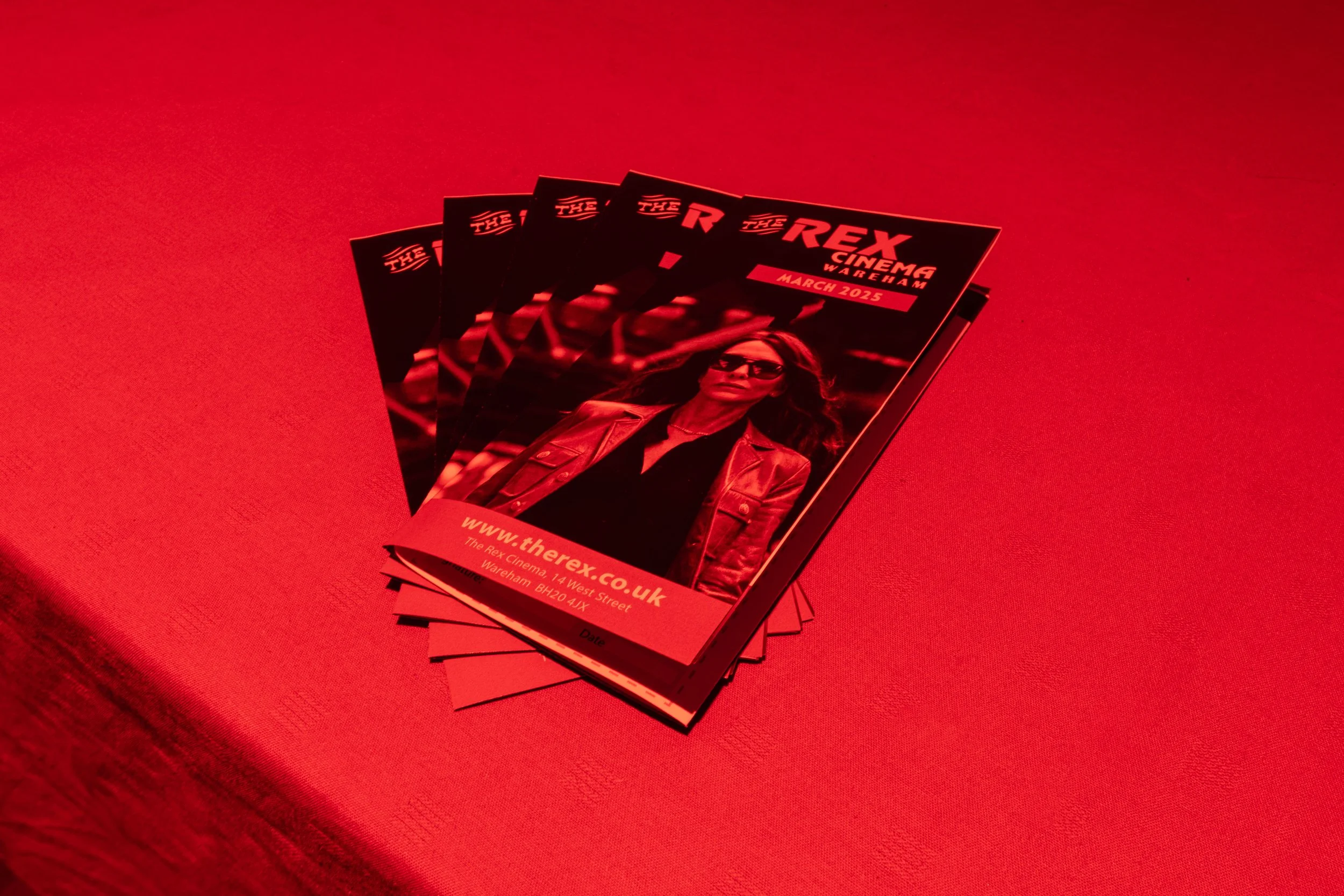 Flyers for the movie 'The Rex' at Rex Cinema Warehouse, March 2025, placed on a red surface.