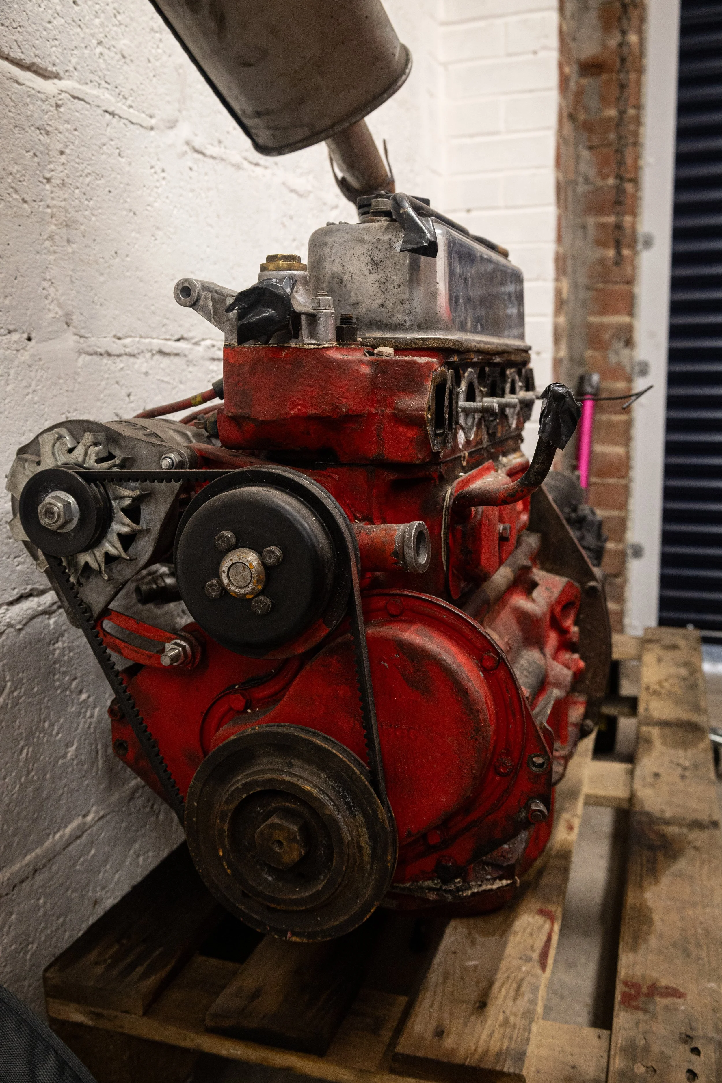 A disassembled red engine placed on a wooden pallet in a workshop with brick and white walls.