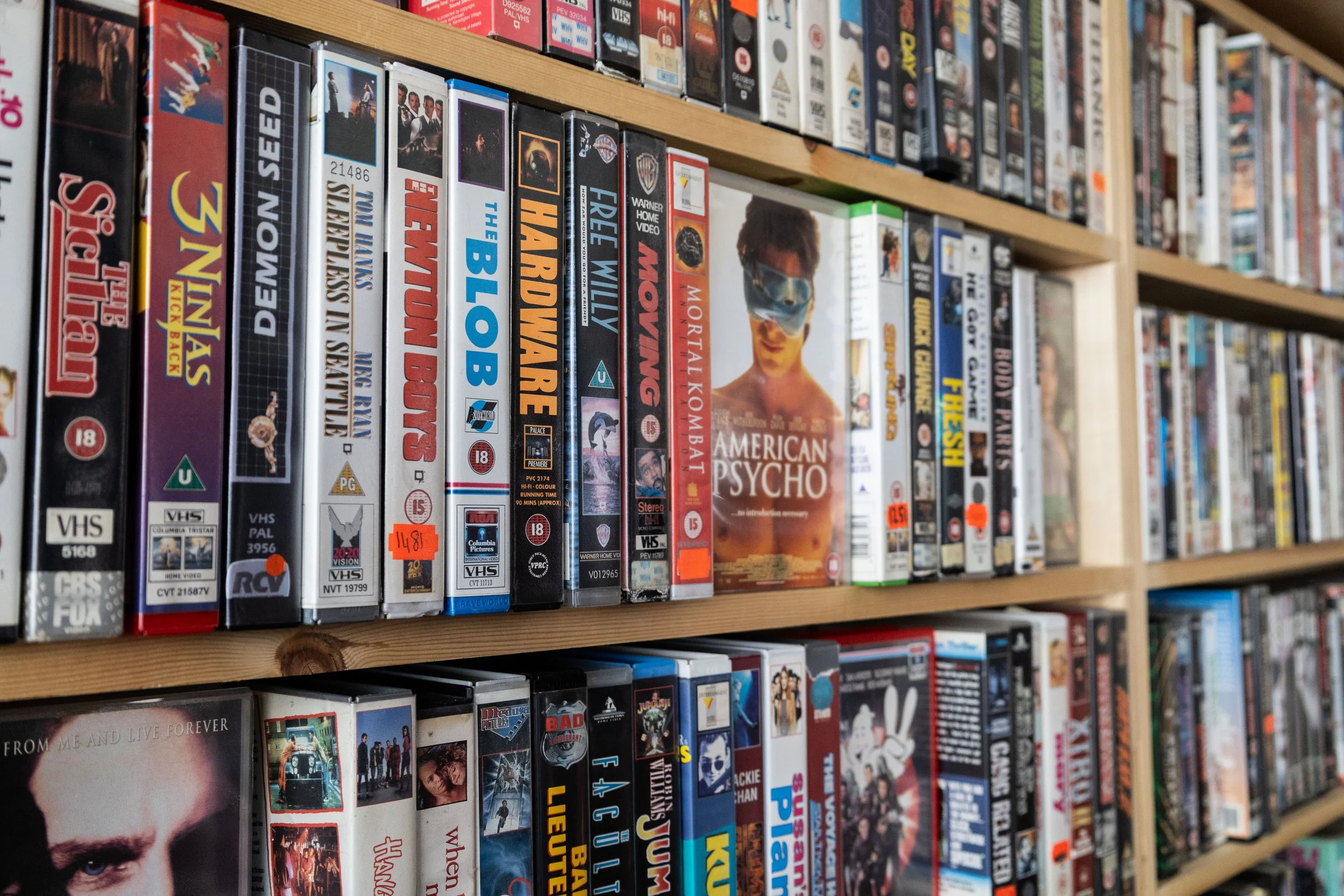 Rows of VHS tapes and DVD boxes on wooden shelves in a store.