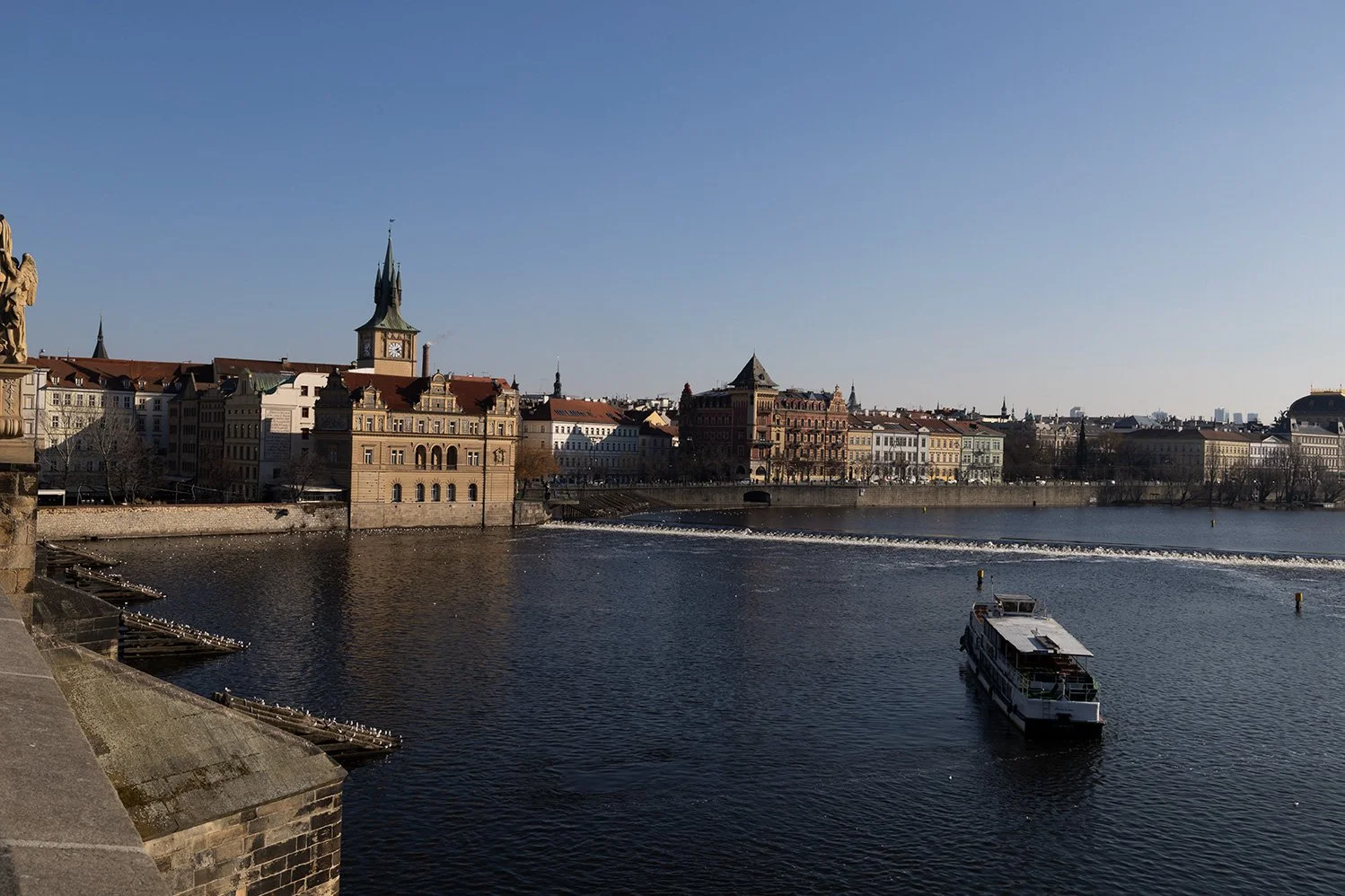 Cityscape along river with boat and historic buildings under clear blue sky.